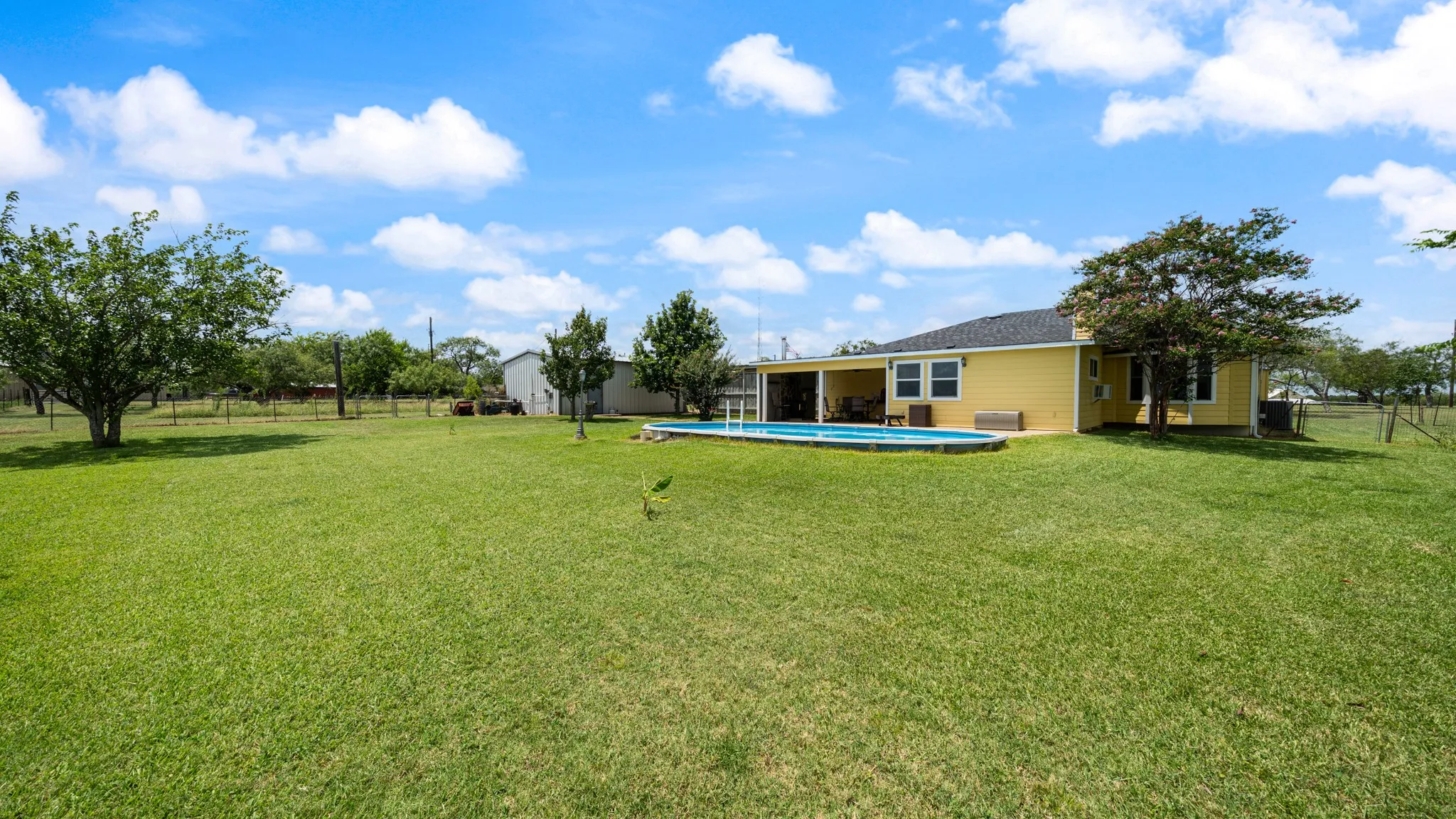 Expansive grassy area with mature trees, an above-ground pool, and a covered patio