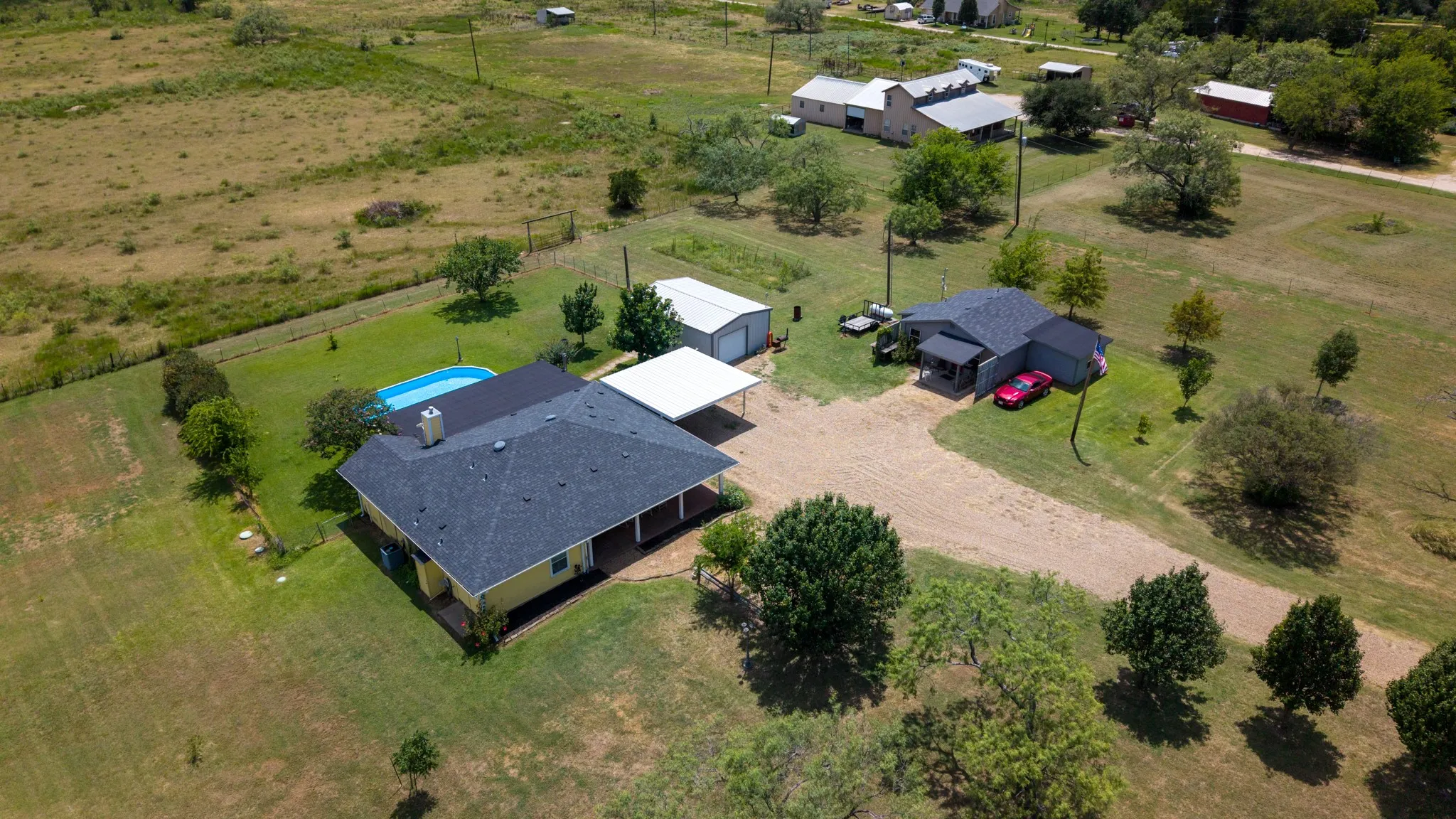 Property featuring two detached residences, an in-ground swimming pool, a covered carport, and multiple outbuildings