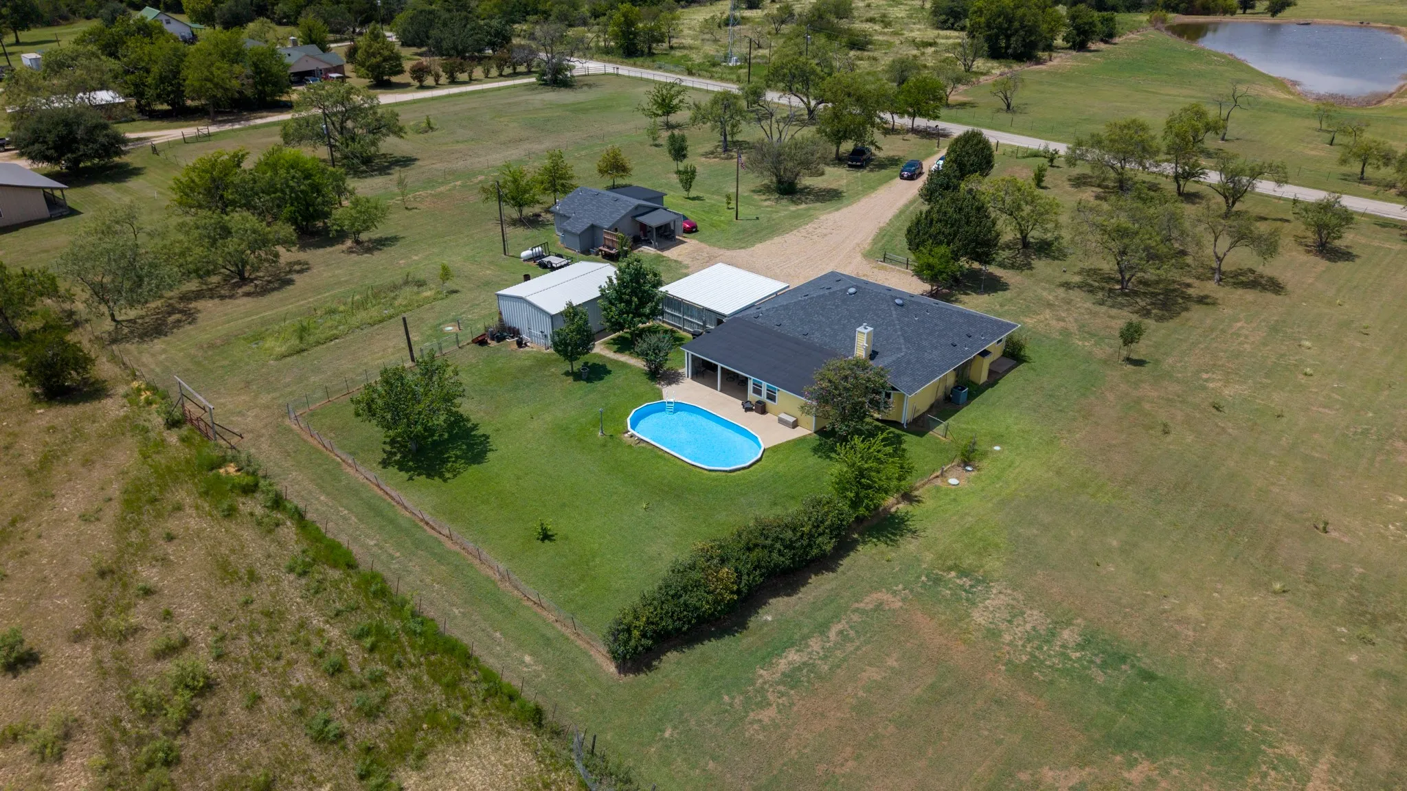 Expansive residential property featuring a modern single-story home with a dark-shingled roof, situated on manicured grounds with mature landscaping