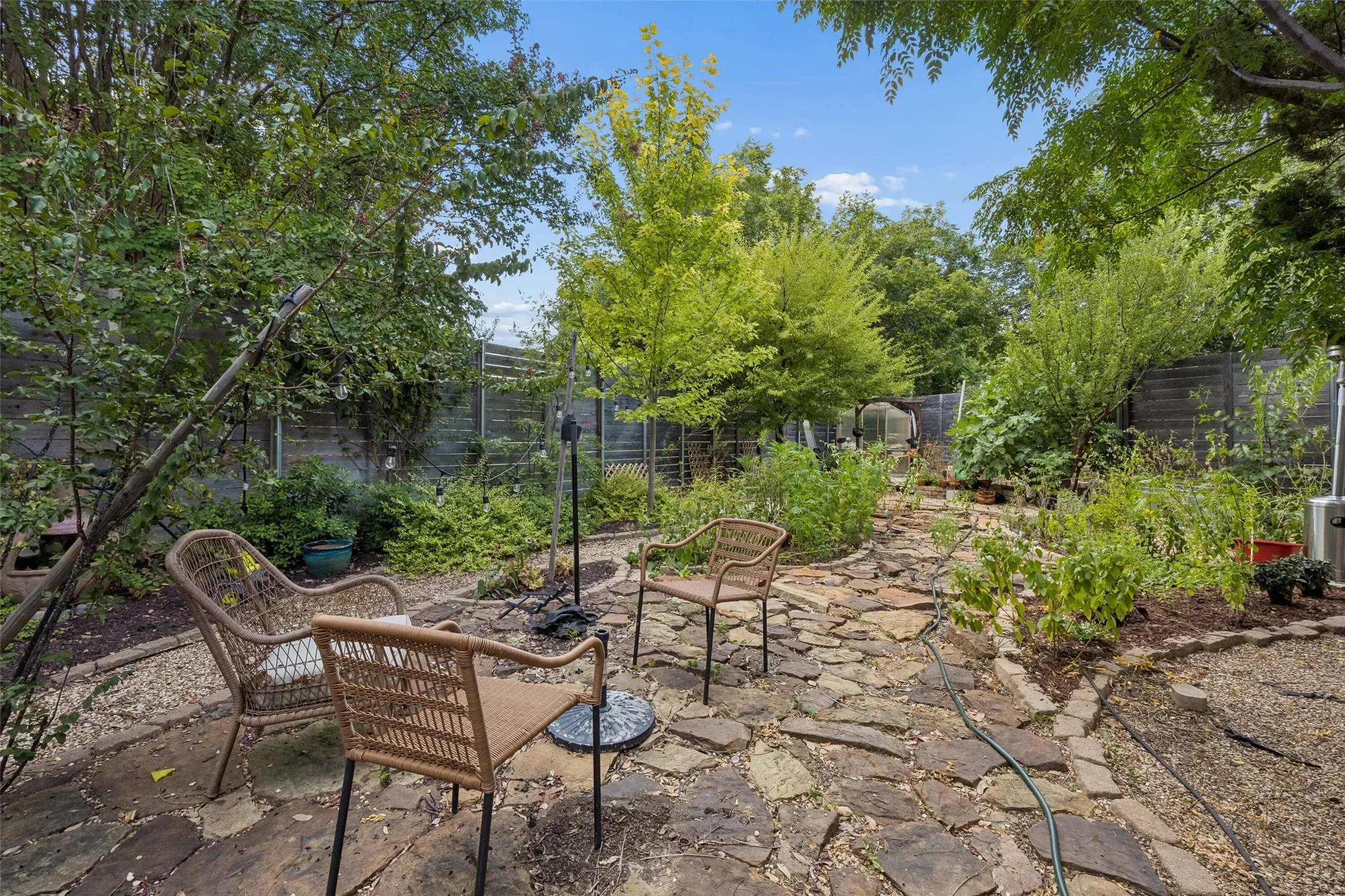 Expansive natural backyard featuring mature trees, a flagstone patio, gravel pathways, and planted garden beds