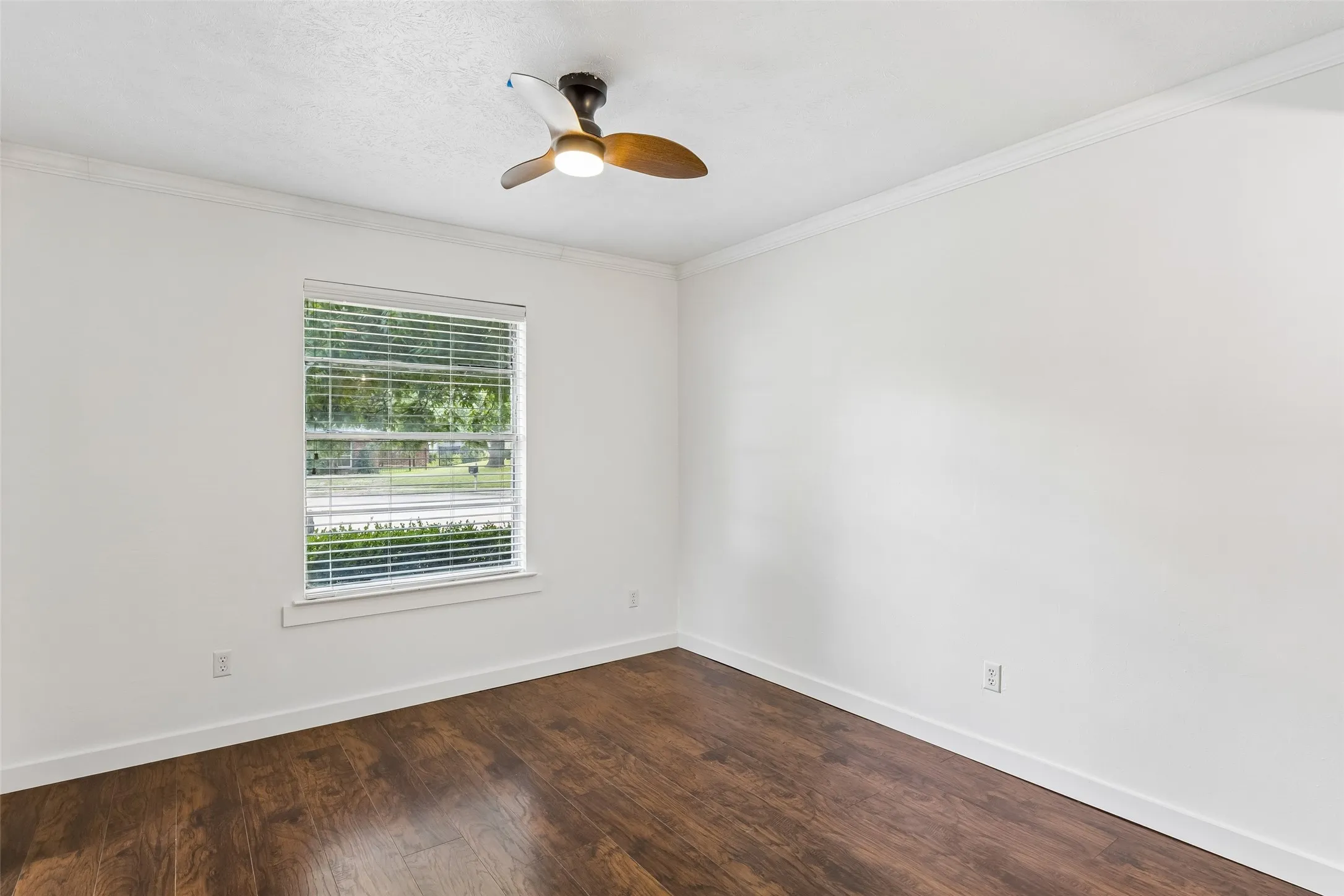 Window with blinds, laminate wood flooring, ceiling fan, crown molding, and white walls