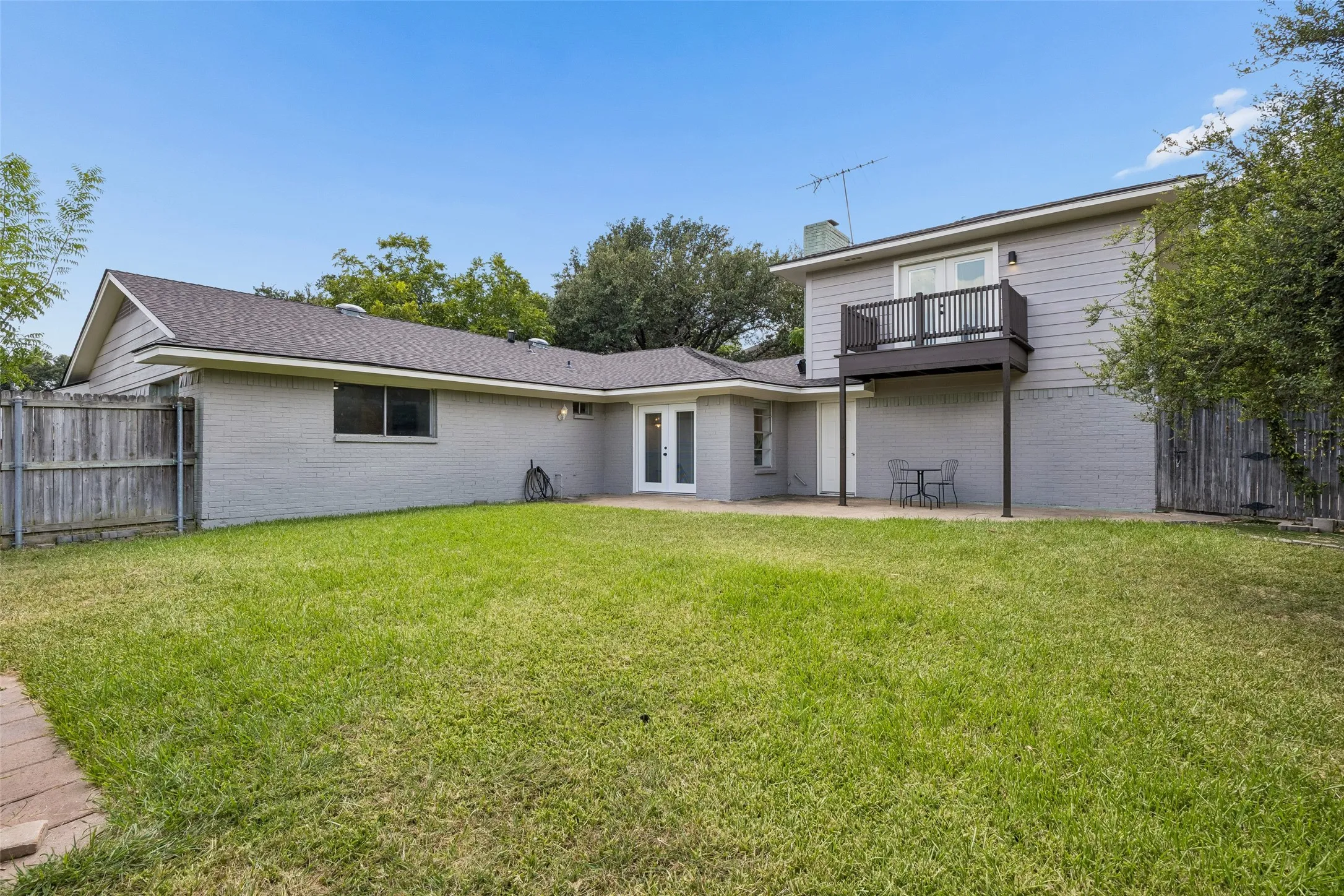 Expansive green lawn with a privacy fence, a ground-level patio, and a second-story balcony