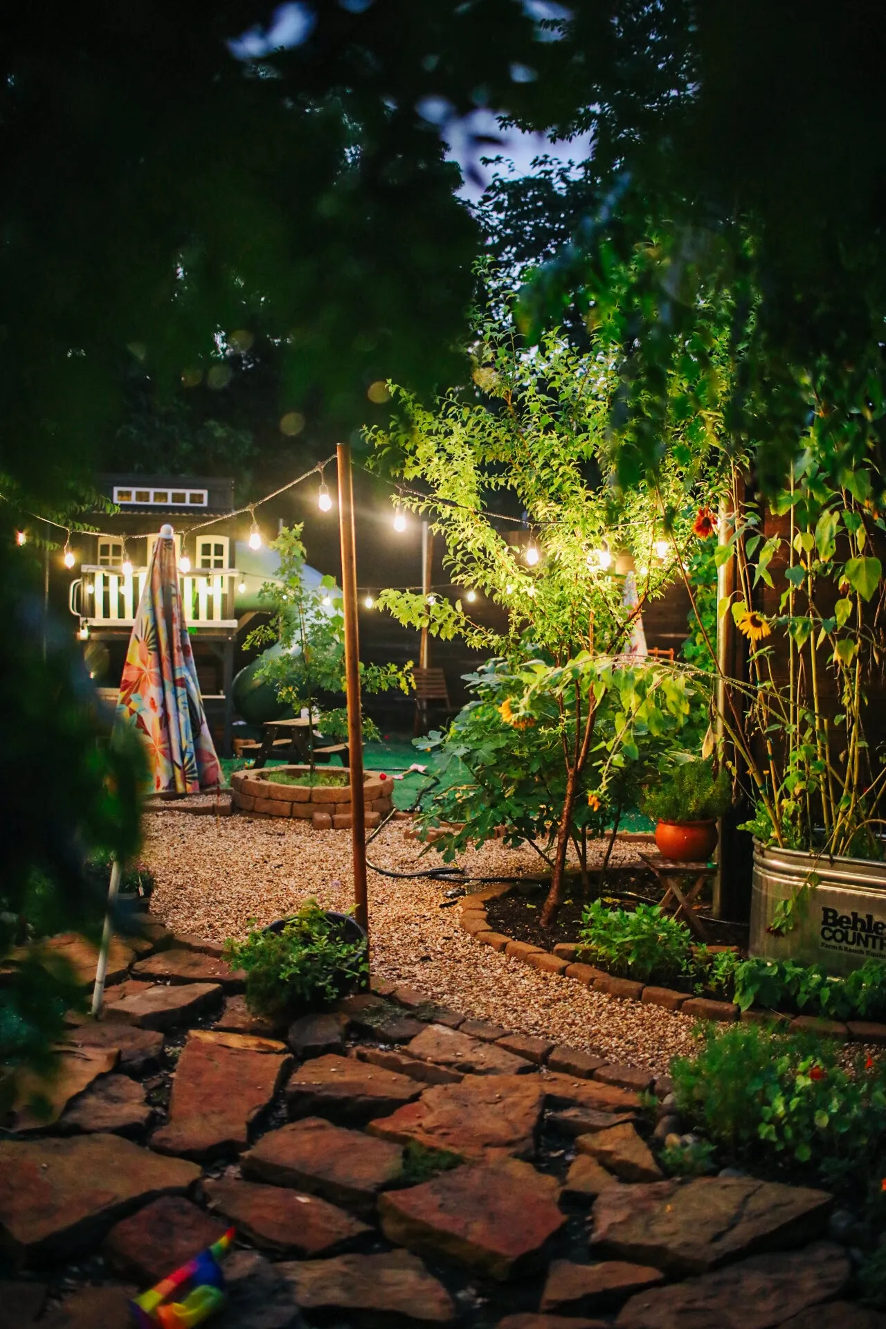 The garden at dusk in full bloom. Flagstone pathway with gravel accents, leading to a circular brick-edged garden bed