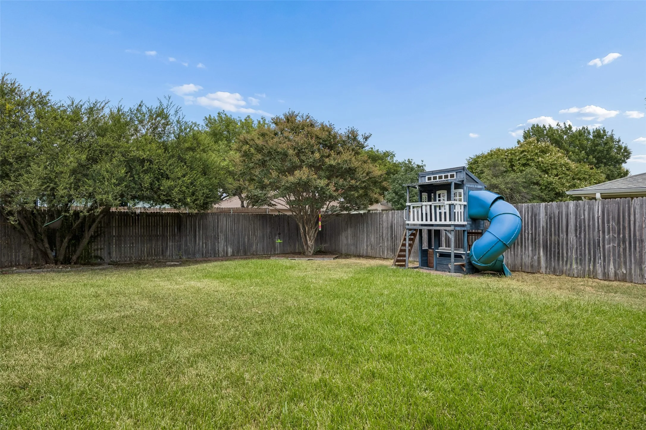Expansive backyard featuring a lush lawn, privacy fencing, and mature trees
