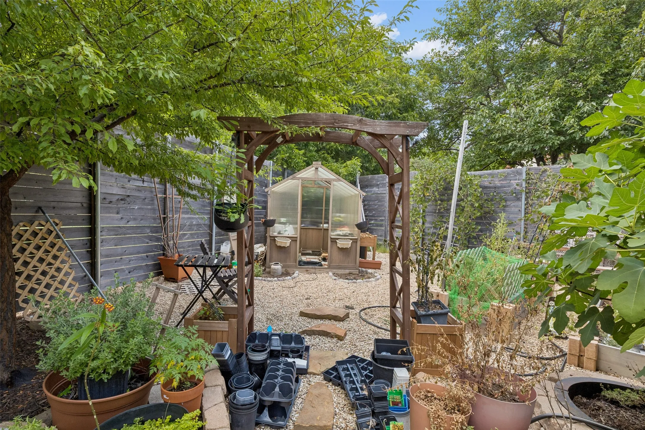 Private garden space featuring a wood arbor, gravel pathways, and a greenhouse structure