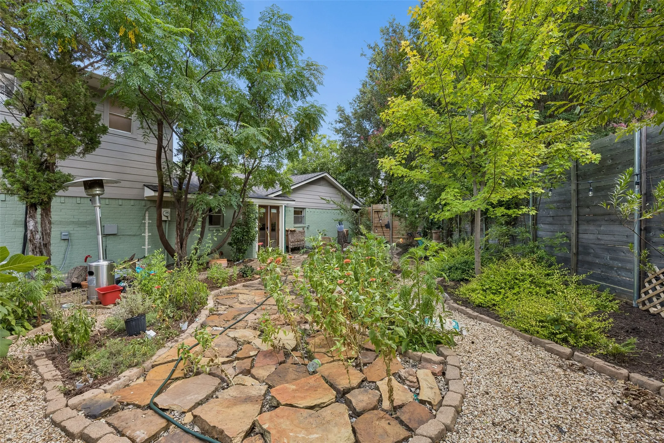 Expansive backyard featuring a natural stone pathway, gravel hardscaping, mature trees, and established plantings