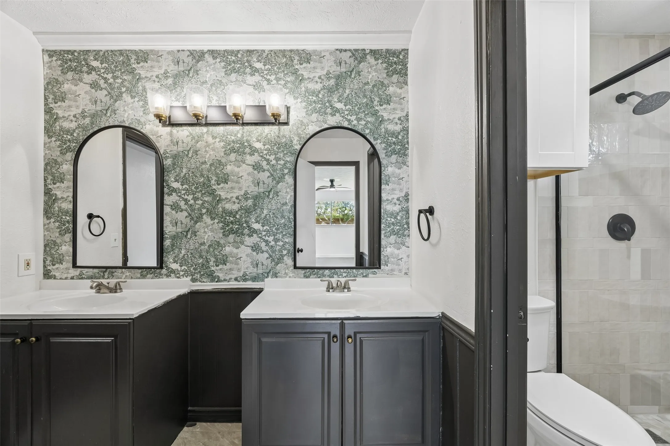 Dual vanities with white countertops, black cabinetry, arched mirrors, and a four-light fixture