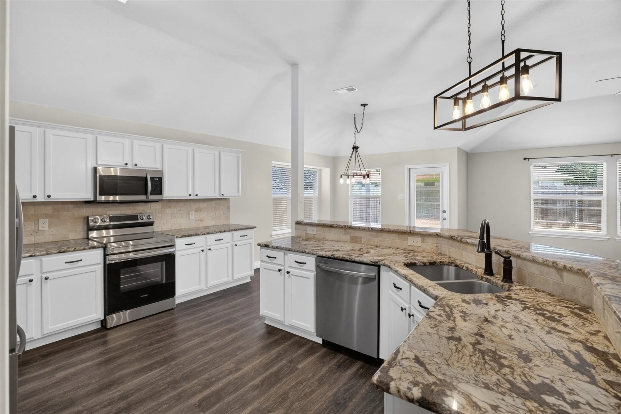Spacious kitchen featuring an expansive breakfast bar, stainless steel appliances, abundant white cabinetry, wood-finish flooring, and vaulted ceilings