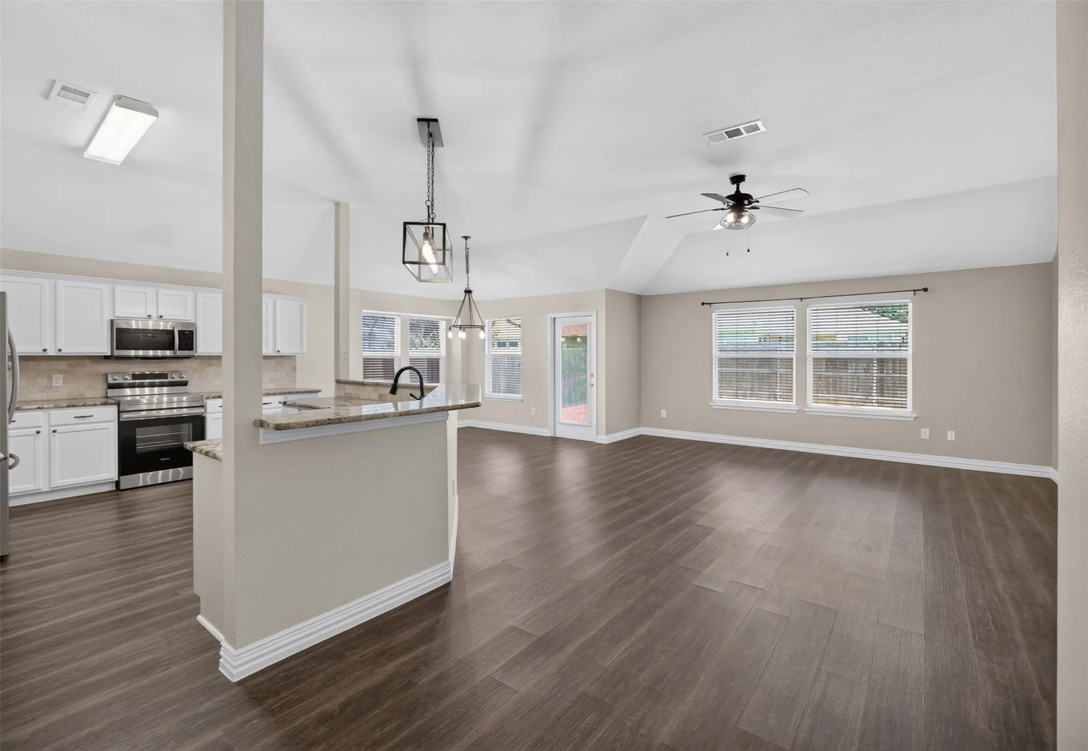 Expansive living area featuring wood-finish flooring, vaulted ceilings, and a ceiling fan