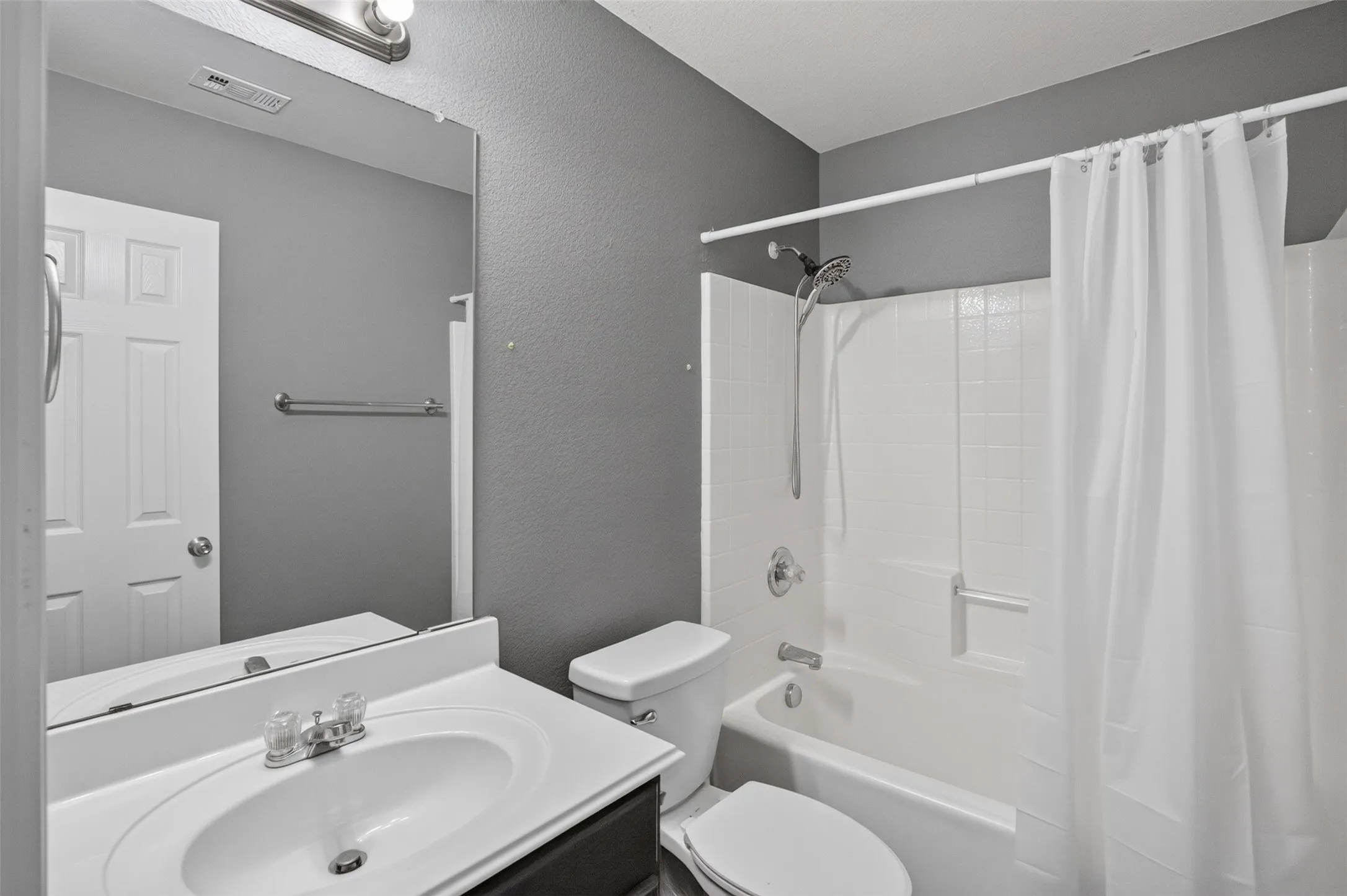 Bathroom featuring a white vanity with an integrated sink, a wall-mounted mirror, a two-piece toilet, and a white tub with a shower fixture and tiled surround
