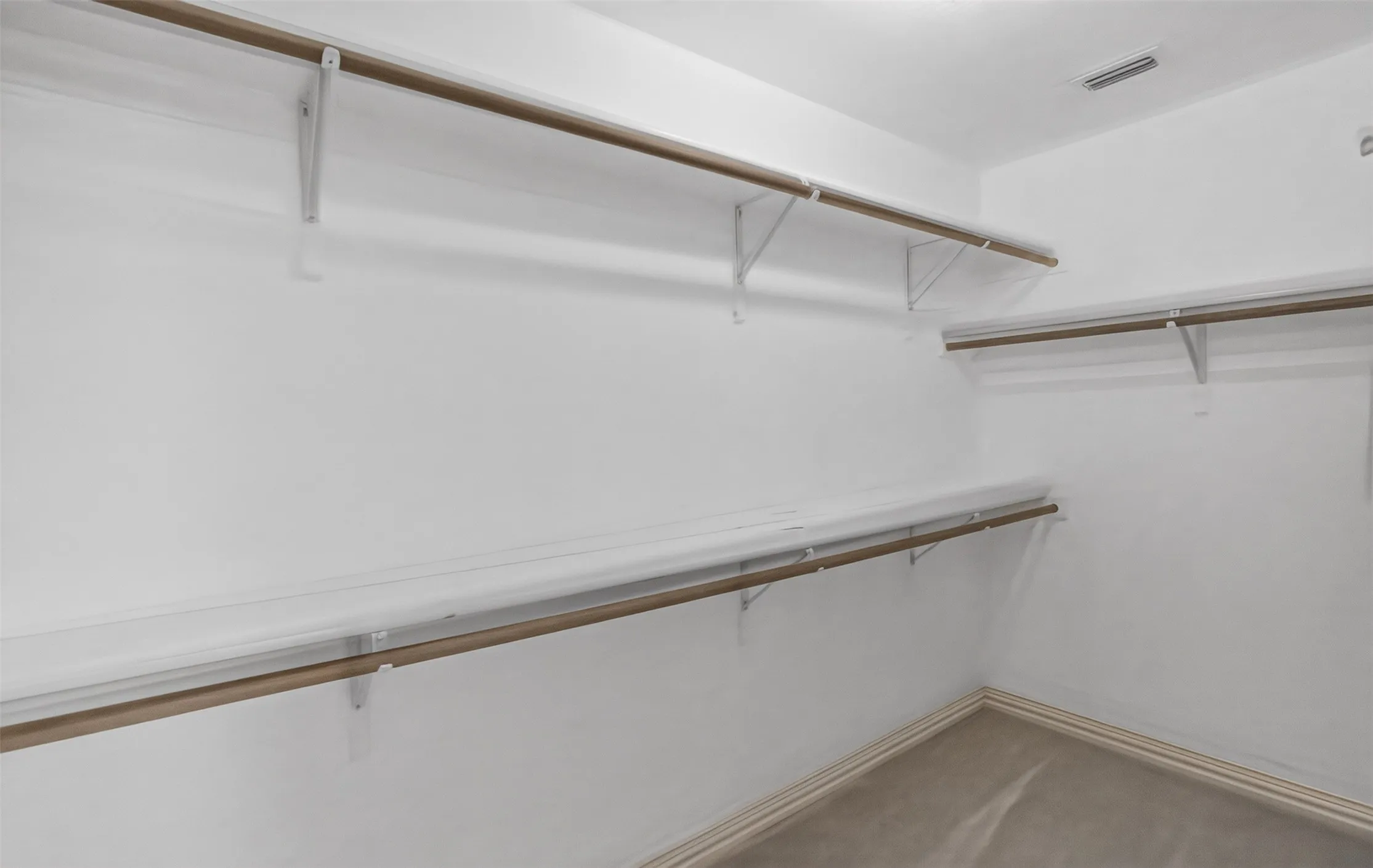 Walk-in closet featuring white shelving, wood-finish hanging rods, white walls, and carpet flooring