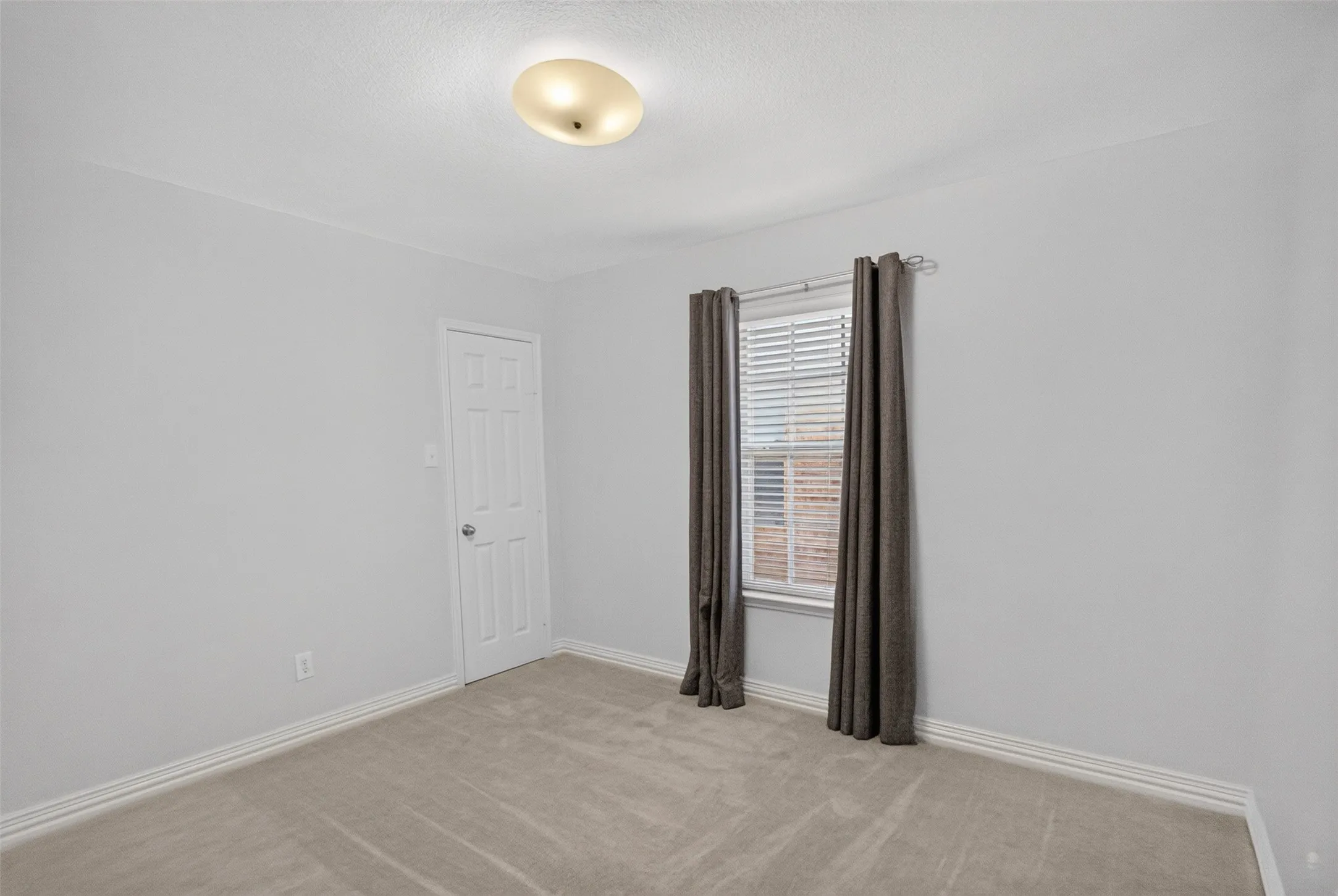 Carpeted room with light gray walls, a white paneled door, and a window with horizontal blinds
