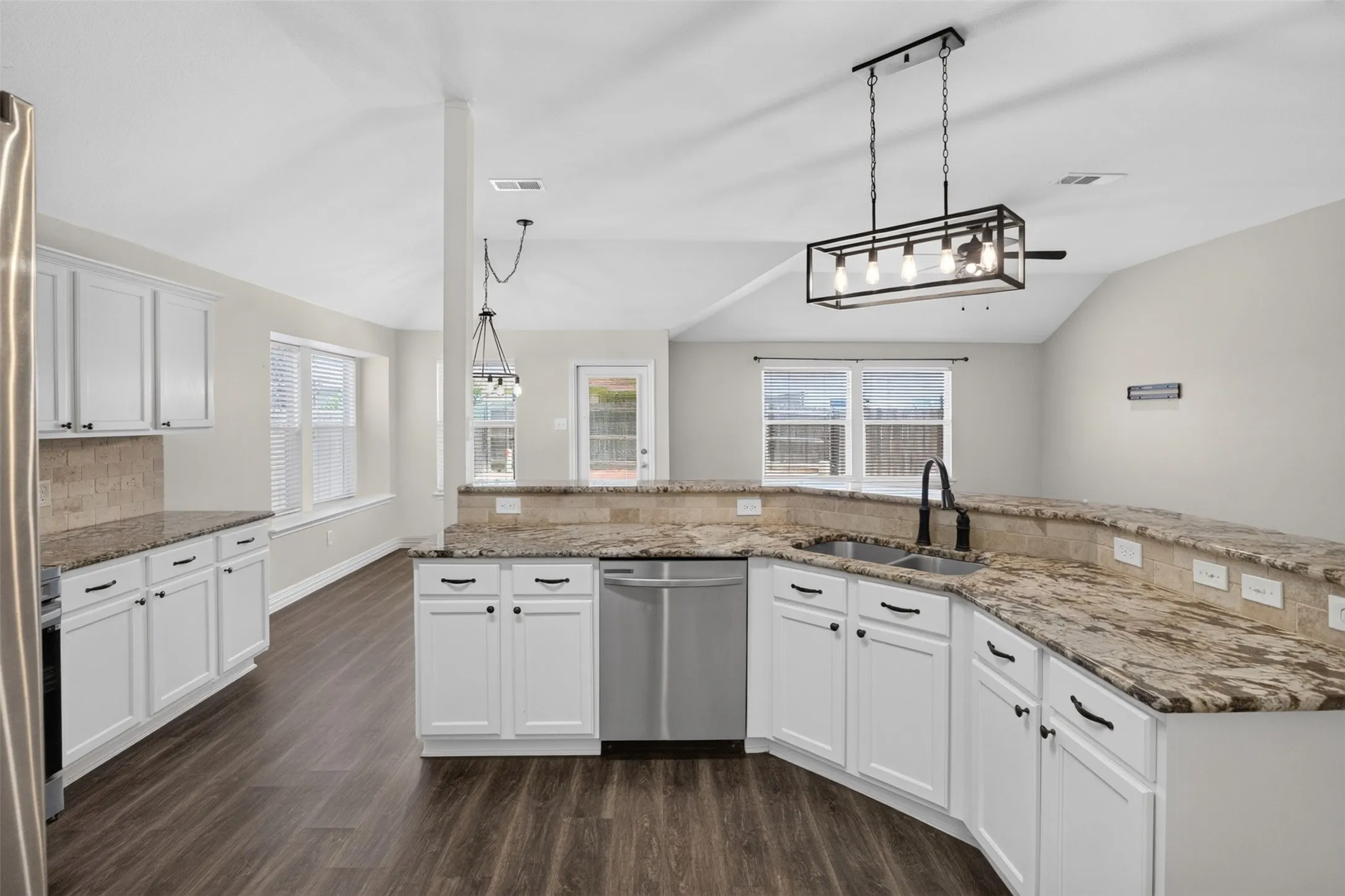 Spacious kitchen featuring white shaker-style cabinetry, granite countertops with waterfall edge detailing, stainless steel appliances including a gas range and dishwasher, and a large center island with seating