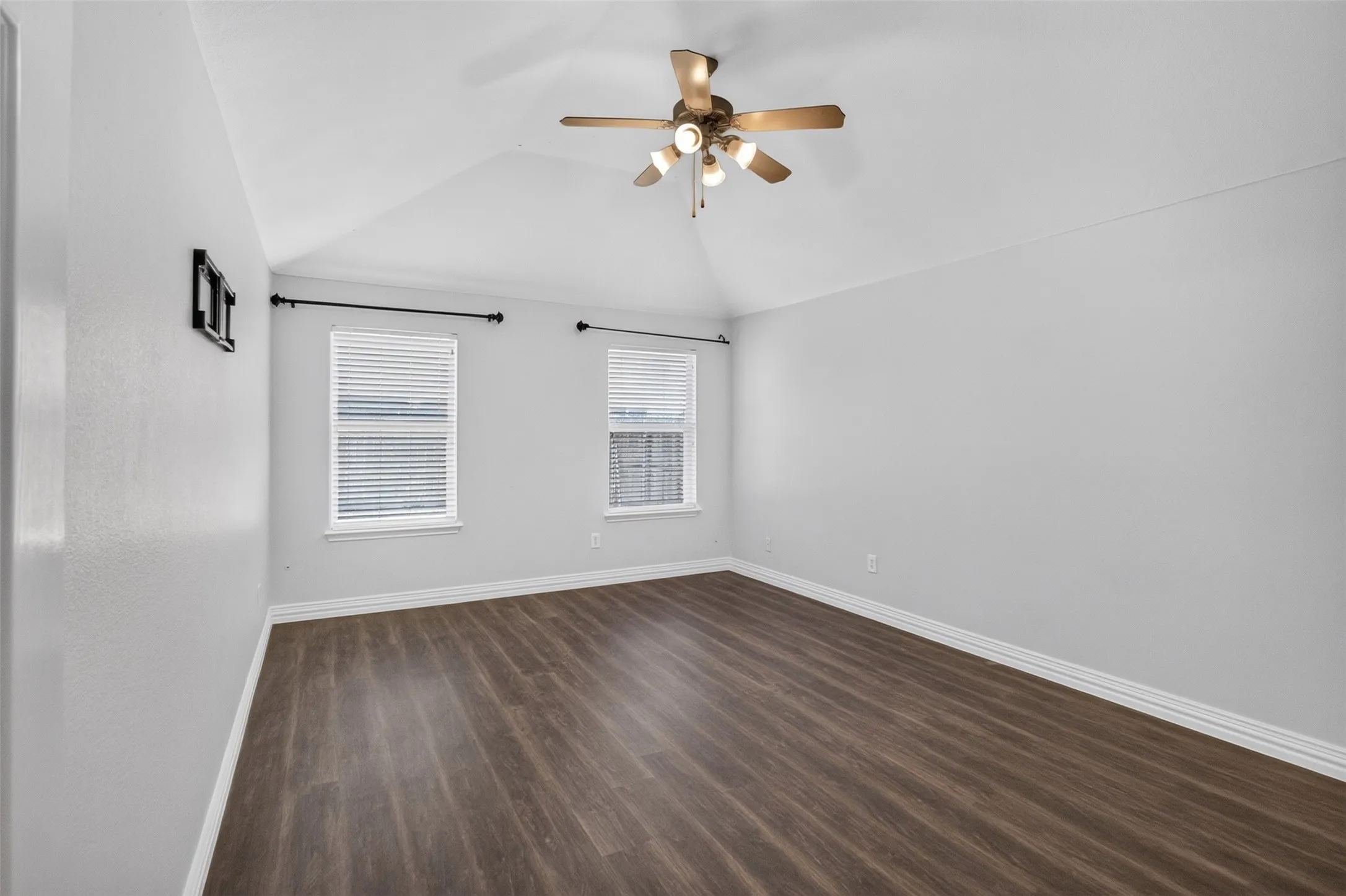 Bright bedroom featuring gleaming wood-finish flooring, white walls, and abundant natural light from two window openings with cellular shades