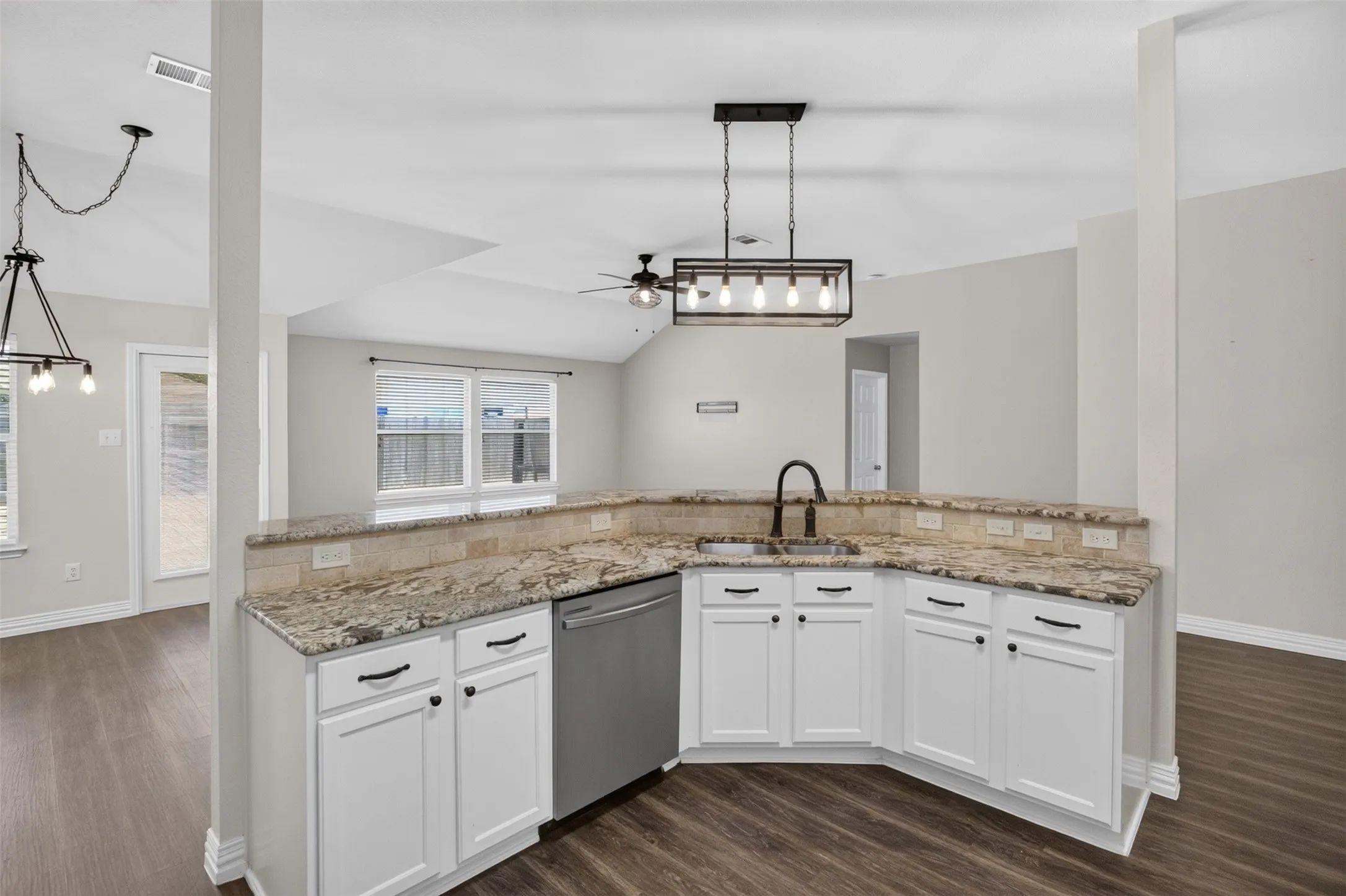 Kitchen featuring white cabinetry, granite countertops, an undermount sink with a gooseneck faucet, a stainless steel dishwasher, and a contemporary linear chandelier