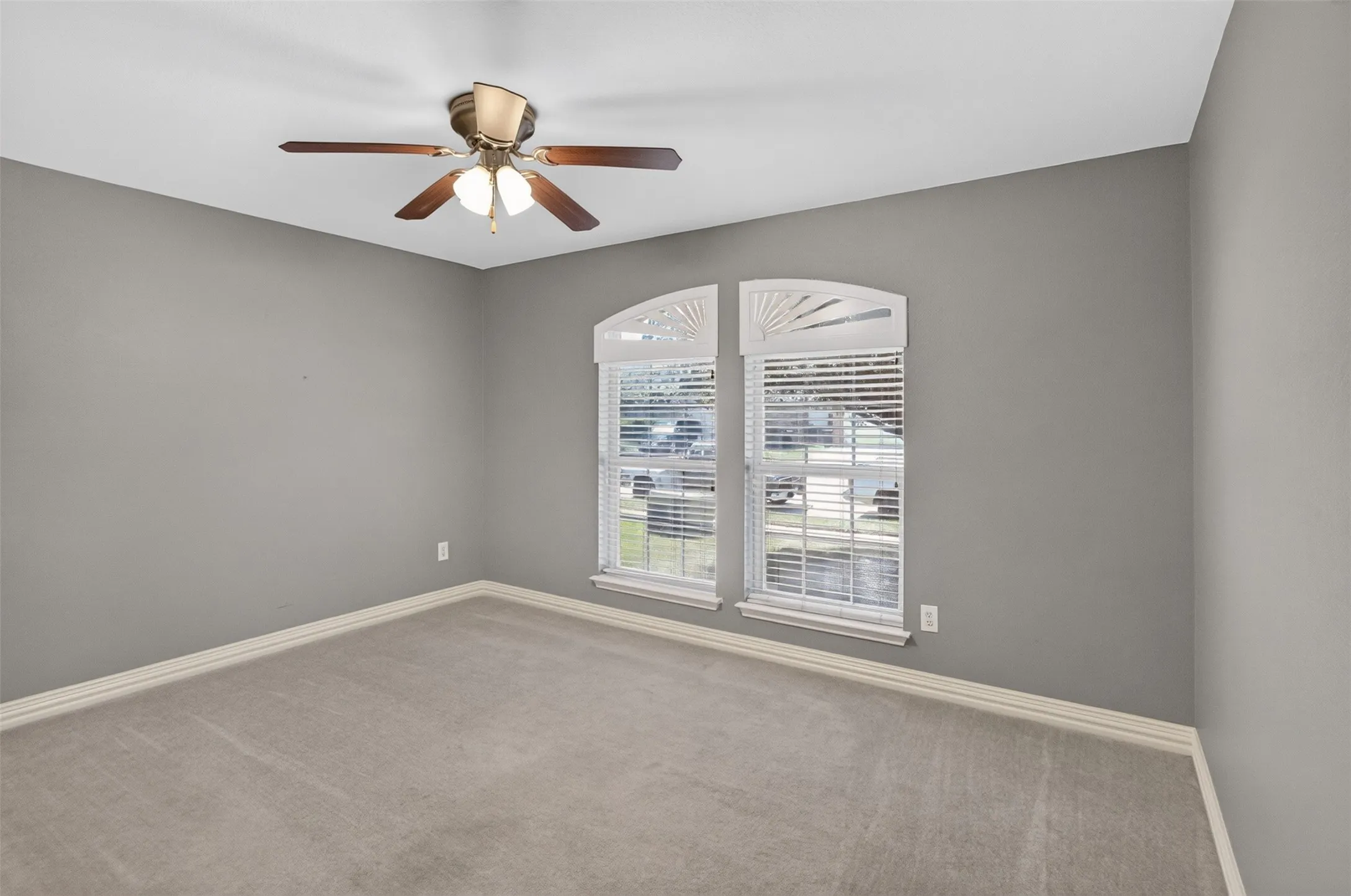 Bedroom featuring twin arched windows with louvered blinds, light gray wall paint, and a ceiling fan with integrated lighting