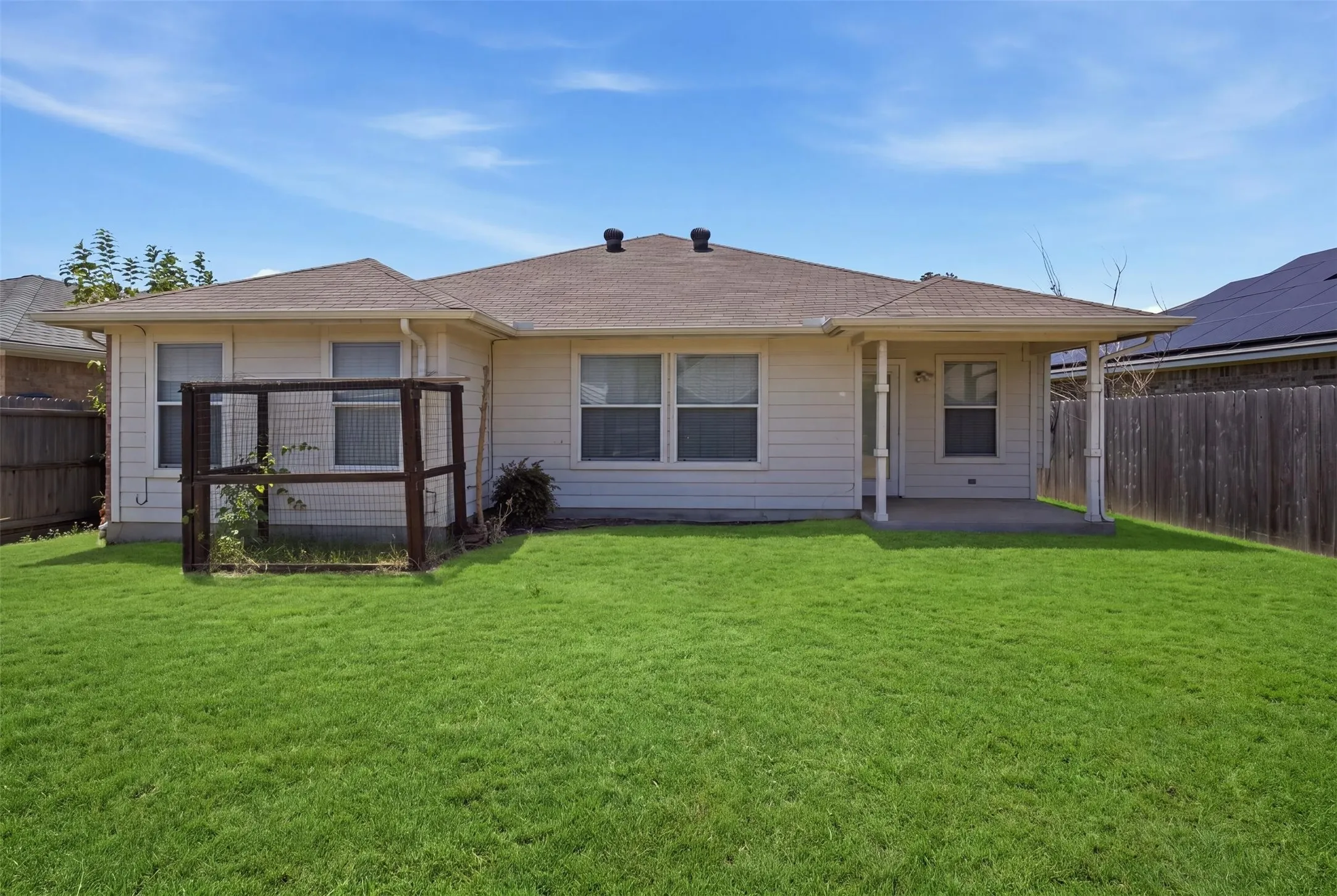 Rear elevation featuring a covered patio, beige siding, white trim, and a fenced backyard with green lawn