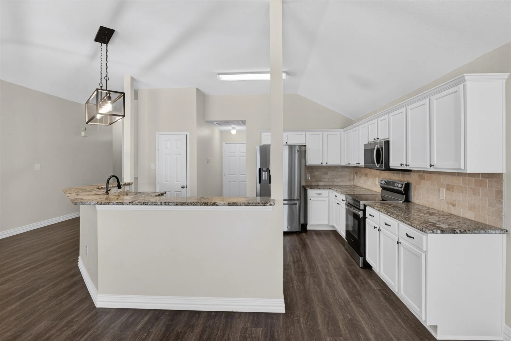 Modern kitchen featuring white cabinetry, dark wood-finish flooring, stainless steel appliances, a stone countertop island with a built-in sink and matte black faucet, and a tiled backsplash