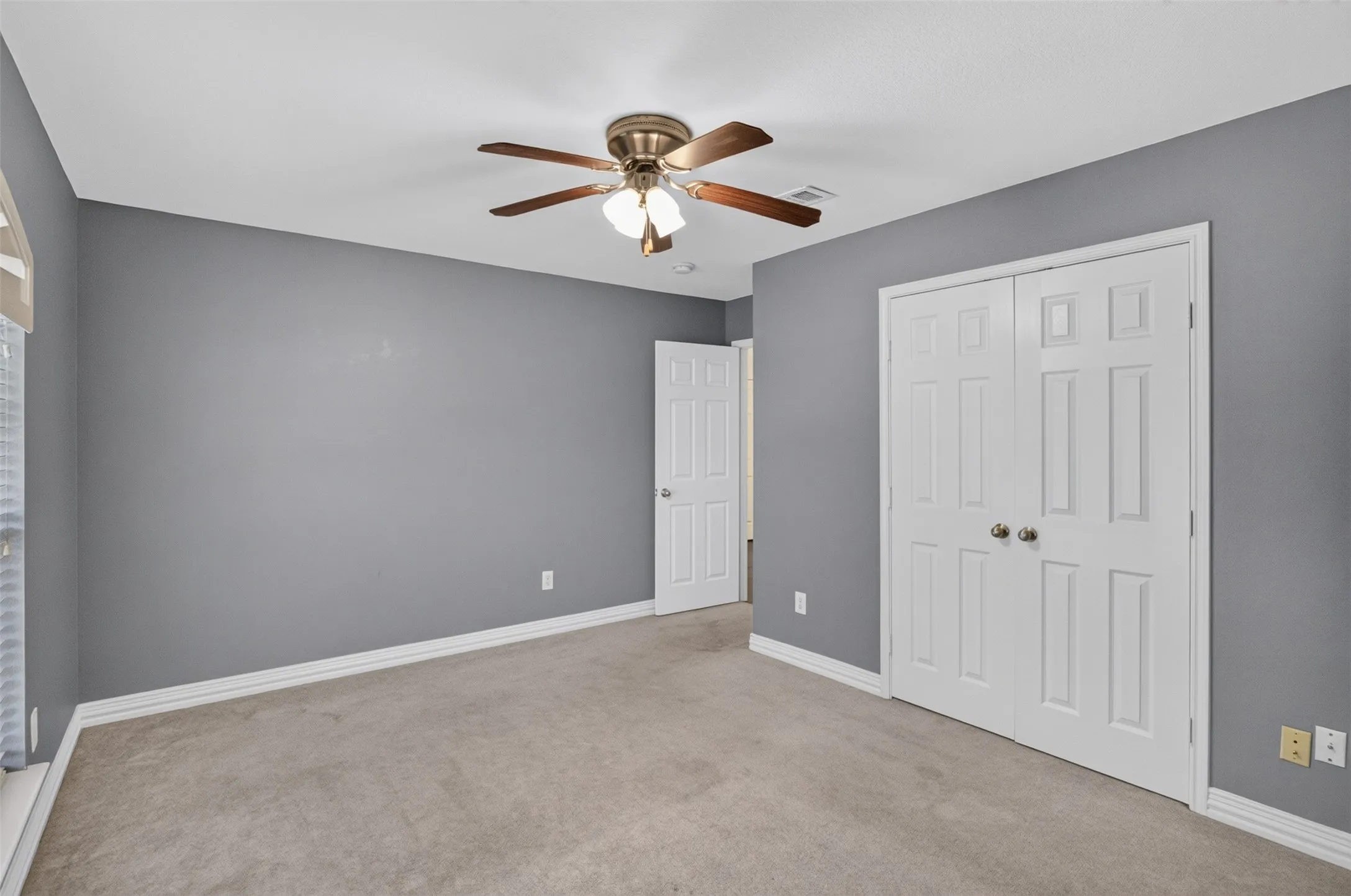 Spacious bedroom showcasing neutral gray walls with crisp white trim, plush carpet flooring, and abundant natural light