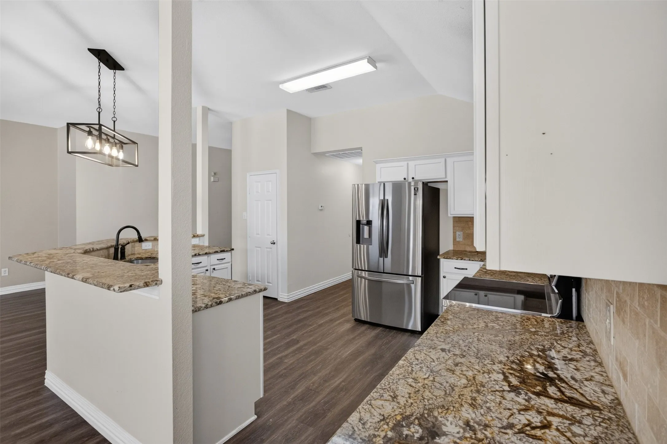 Modern kitchen featuring a large center island with granite countertop, stainless steel French-door refrigerator, wood-finish flooring throughout, recessed and pendant lighting, and ample cabinetry