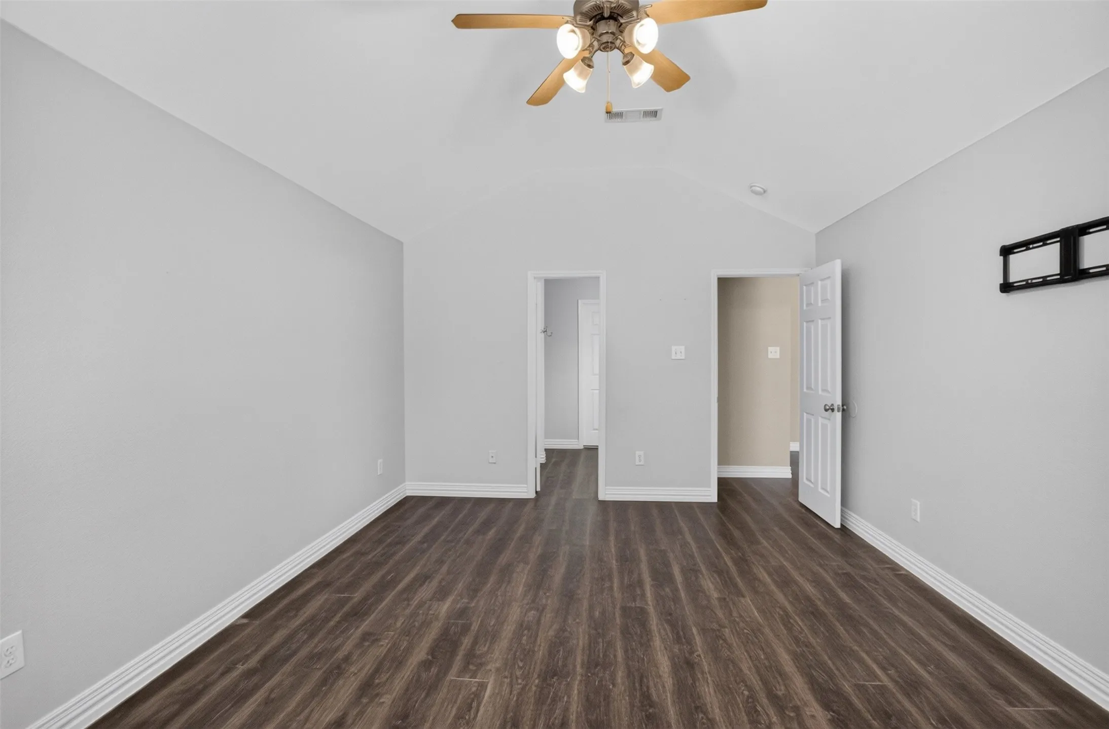 Spacious room featuring wood-finish flooring, vaulted ceiling, and a ceiling fan with integrated lighting