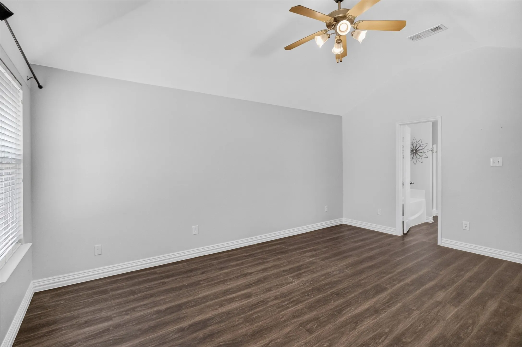 Spacious bedroom showcasing wood-finish flooring, neutral wall finishes, ceiling fan with integrated lighting, and abundant natural light from large window