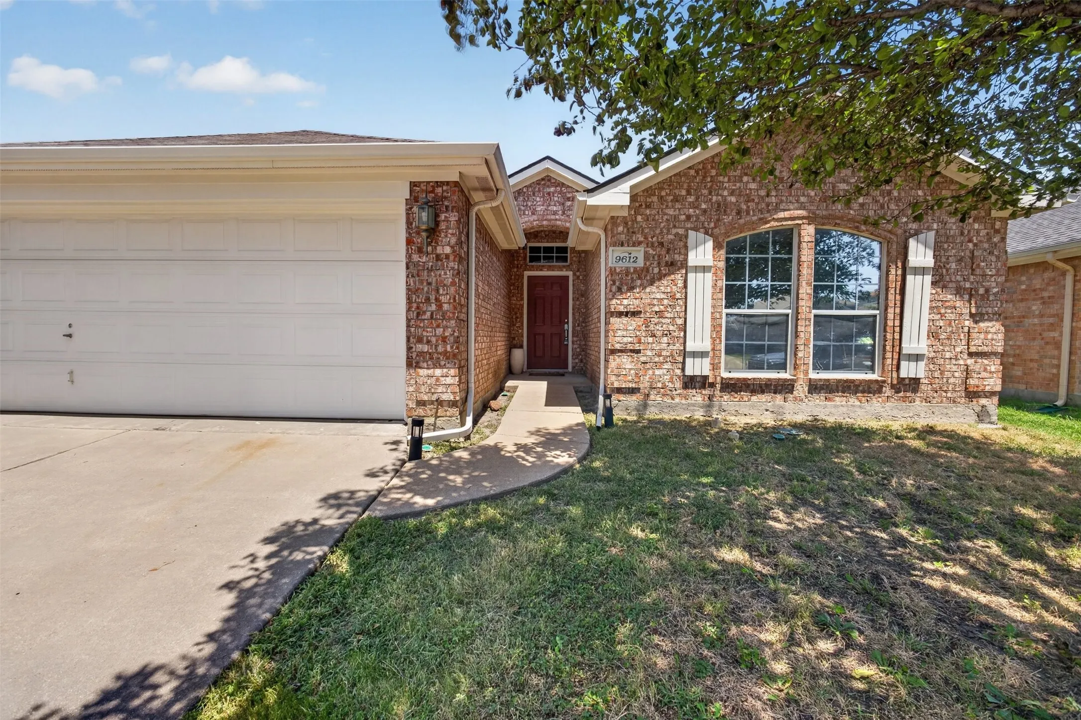 Charming brick home featuring a welcoming front elevation with arched entryway, multi-pane windows with decorative trim, and a two-car garage