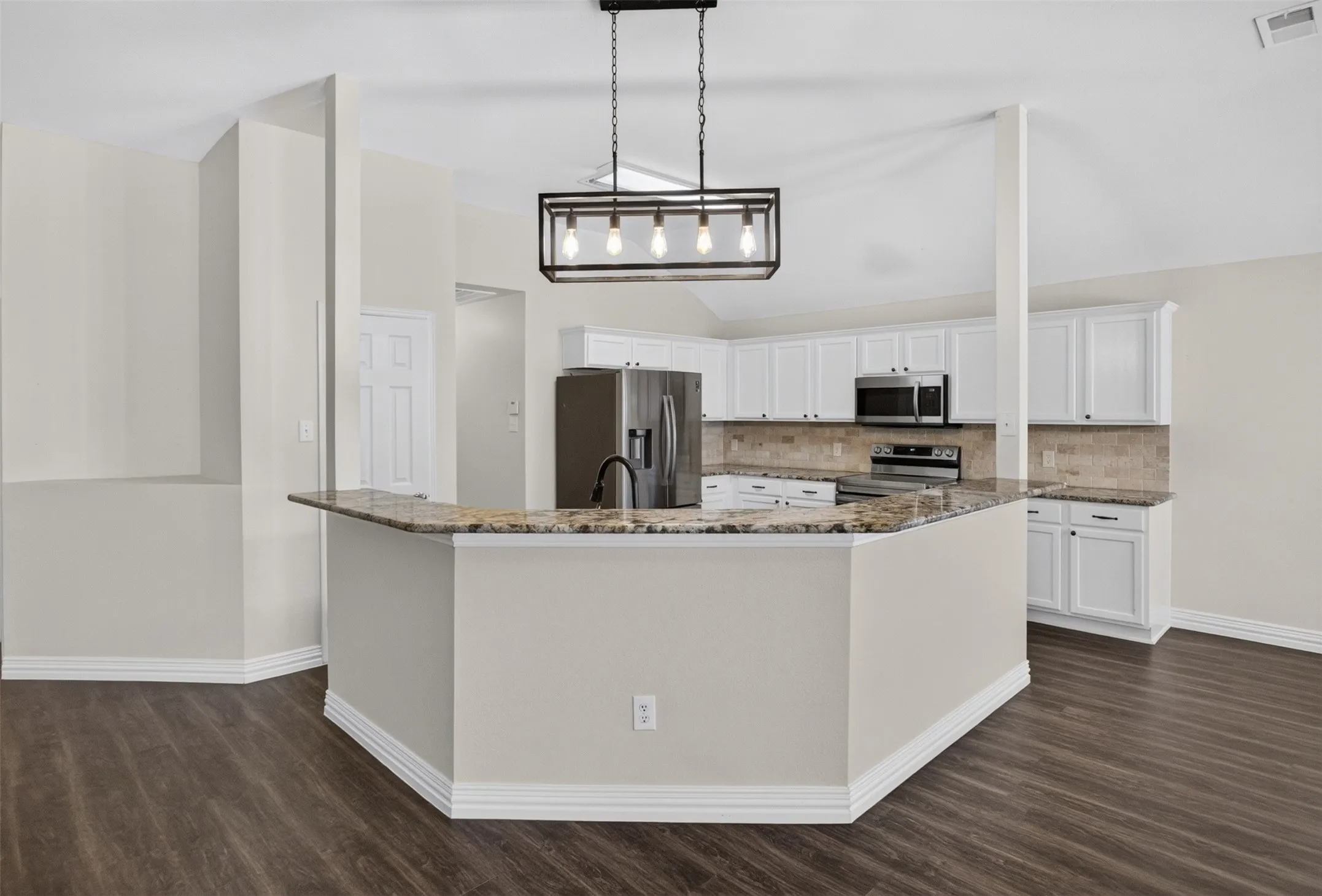 Spacious kitchen featuring an angular breakfast bar with stone countertop, white cabinetry, dark wood-finish flooring, and a contemporary linear chandelier