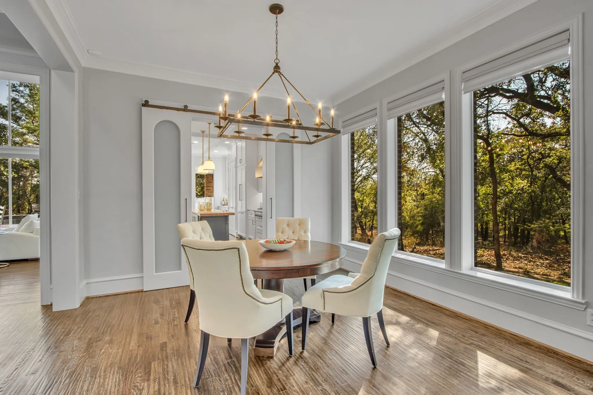 Elegant dining room bathed in natural light from expansive multi-panel windows framing mature woodland scenery.