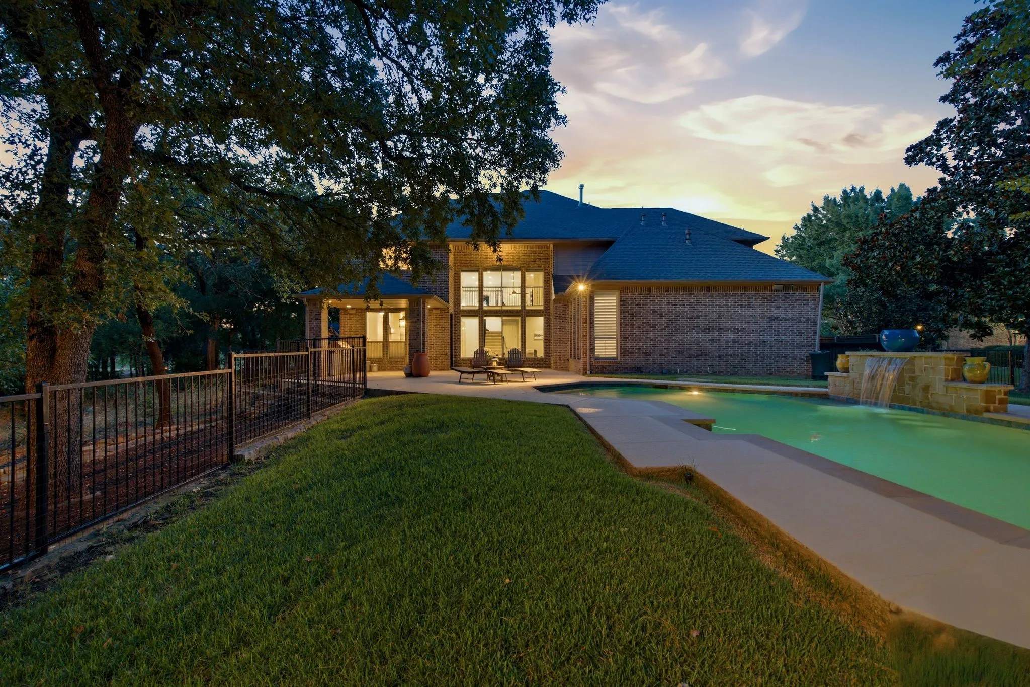 Expansive backyard featuring a rectangular swimming pool with a stone waterfall, patio area, and mature​​‌​​​​‌​​‌‌​‌‌​​​‌‌​‌​‌​‌​​​‌​​ trees