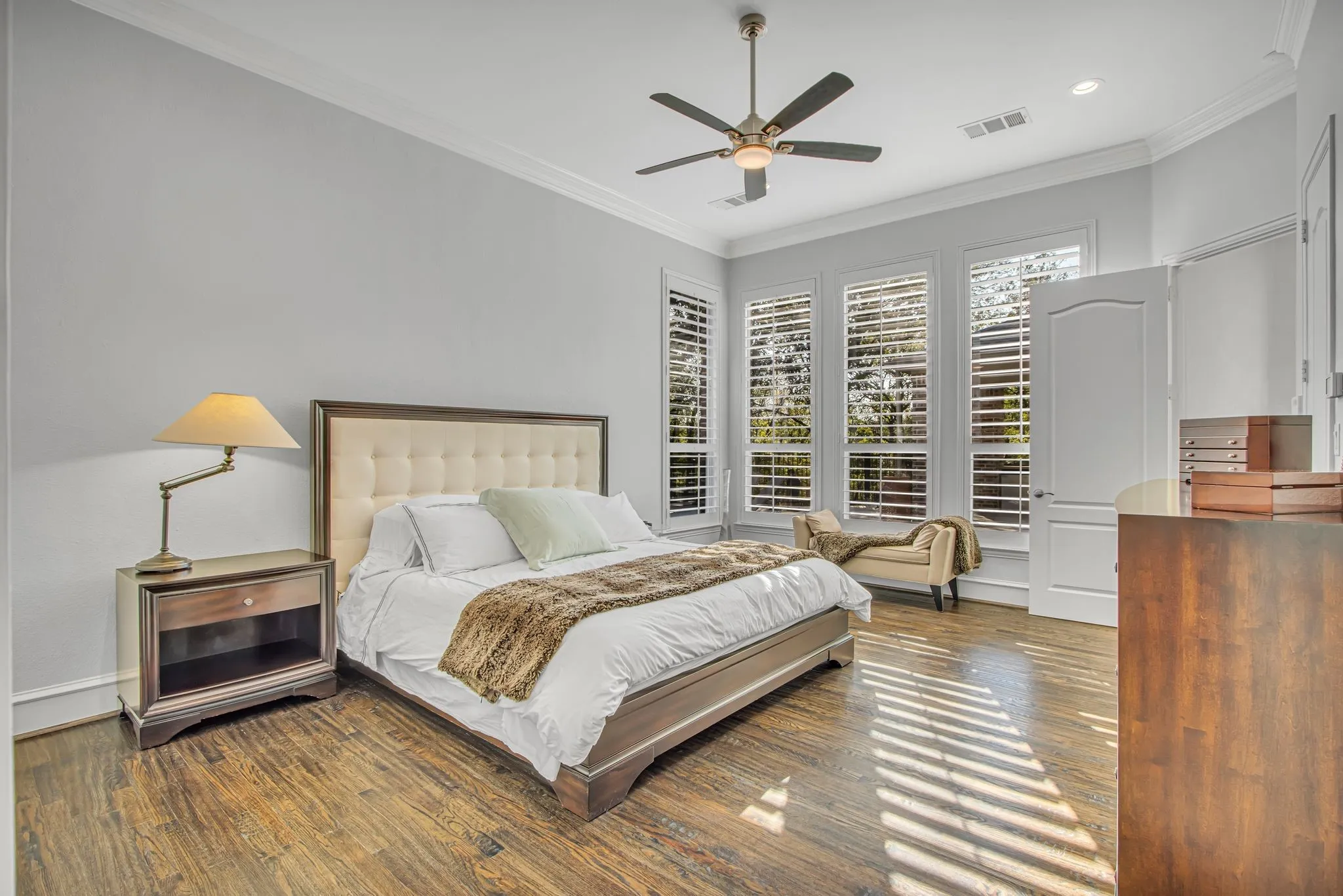Spacious primary bedroom showcasing abundant natural light from multiple plantation shuttered windows.