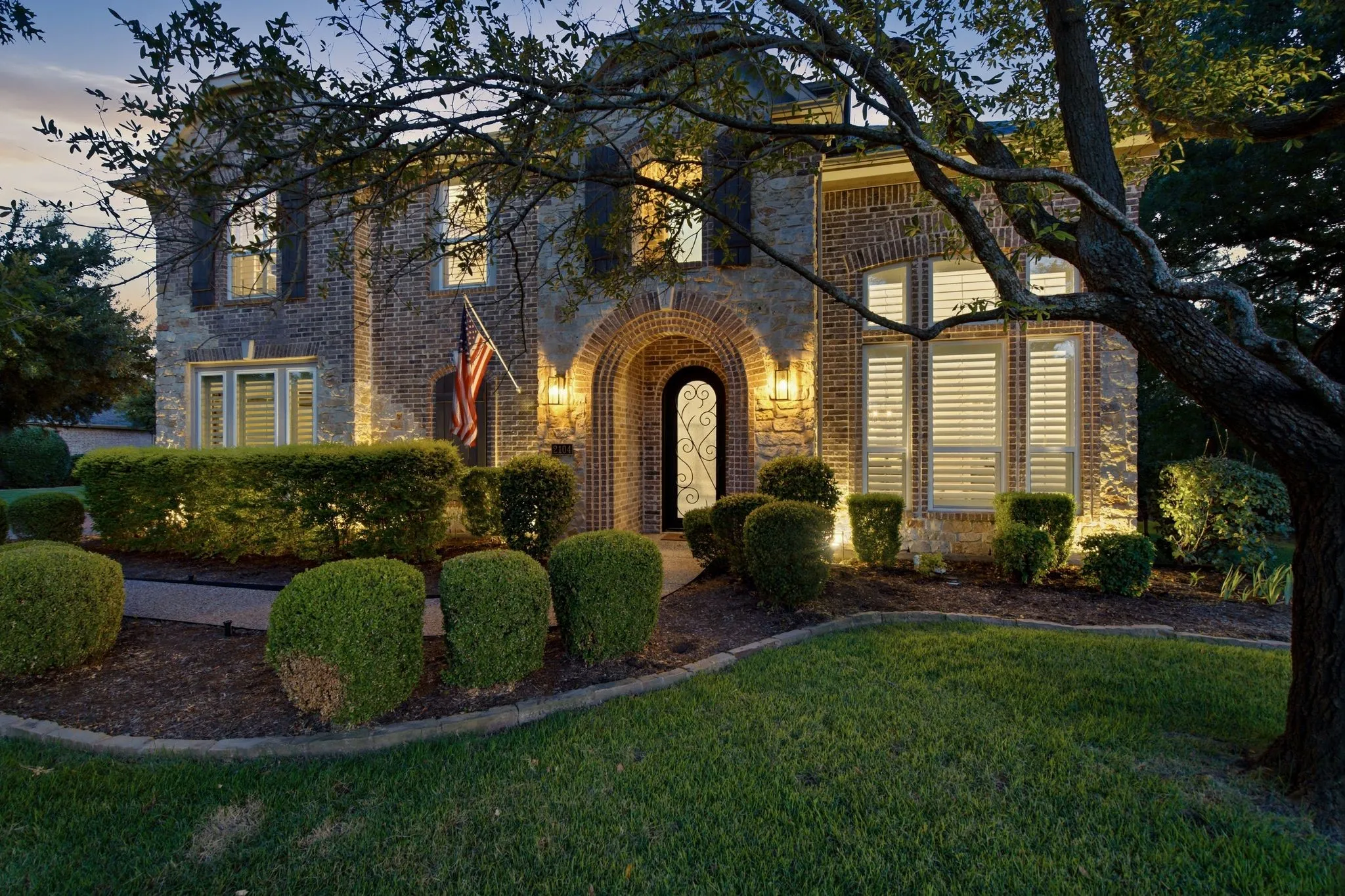 Elegant stone exterior with arched entryway and professional landscape lighting.