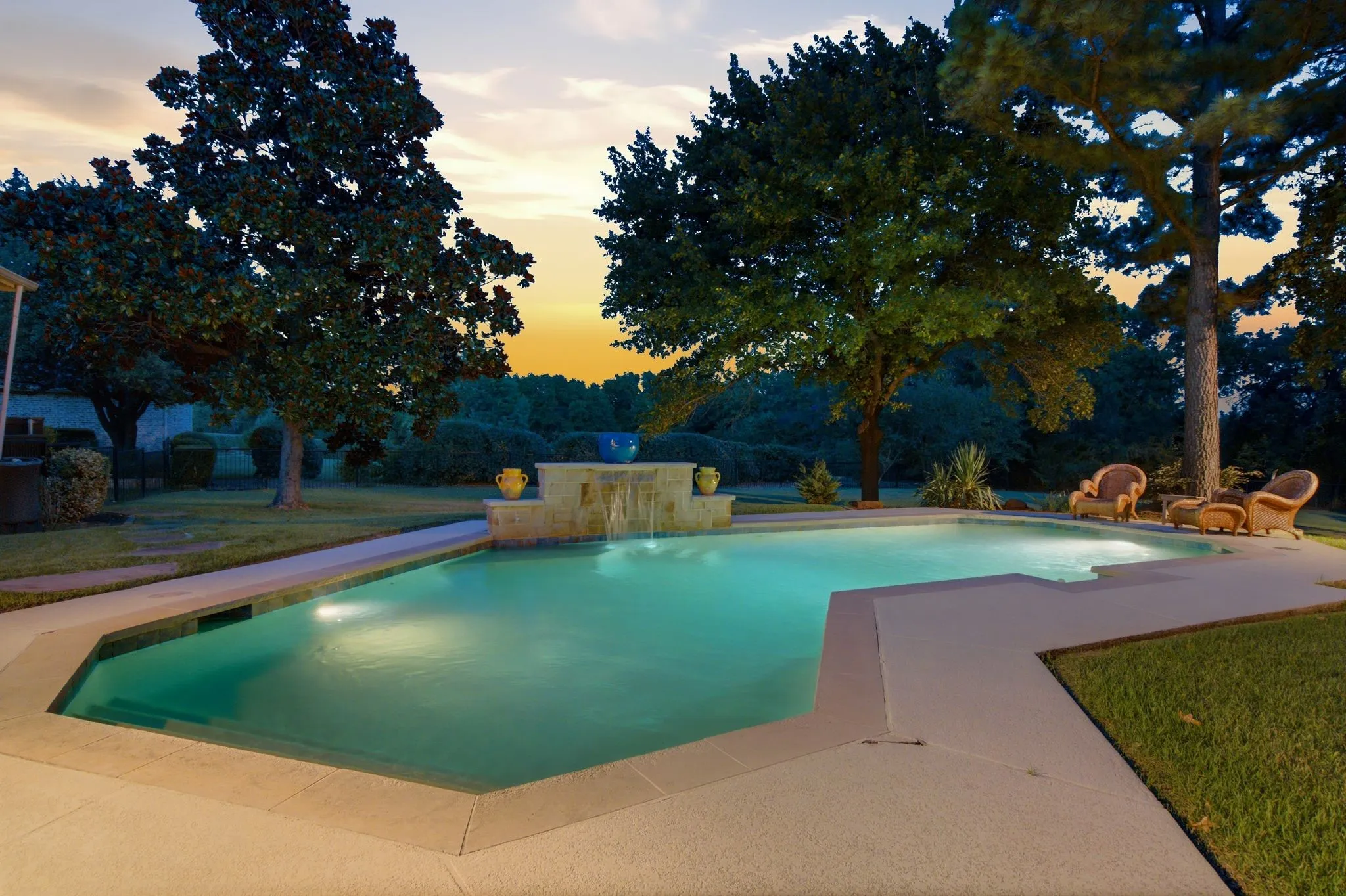 Custom-shaped swimming pool featuring lighting & a stone-clad waterfall feature.