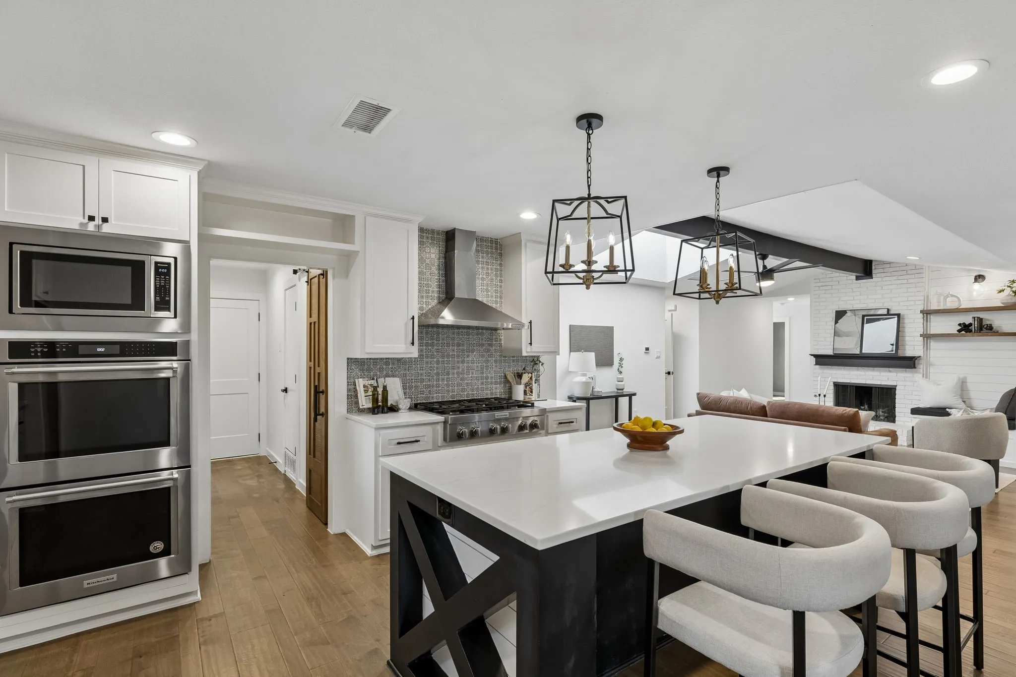Gourmet kitchen featuring stainless steel appliances, a range hood, white cabinetry, a large central island with a white countertop, and wood-finish flooring