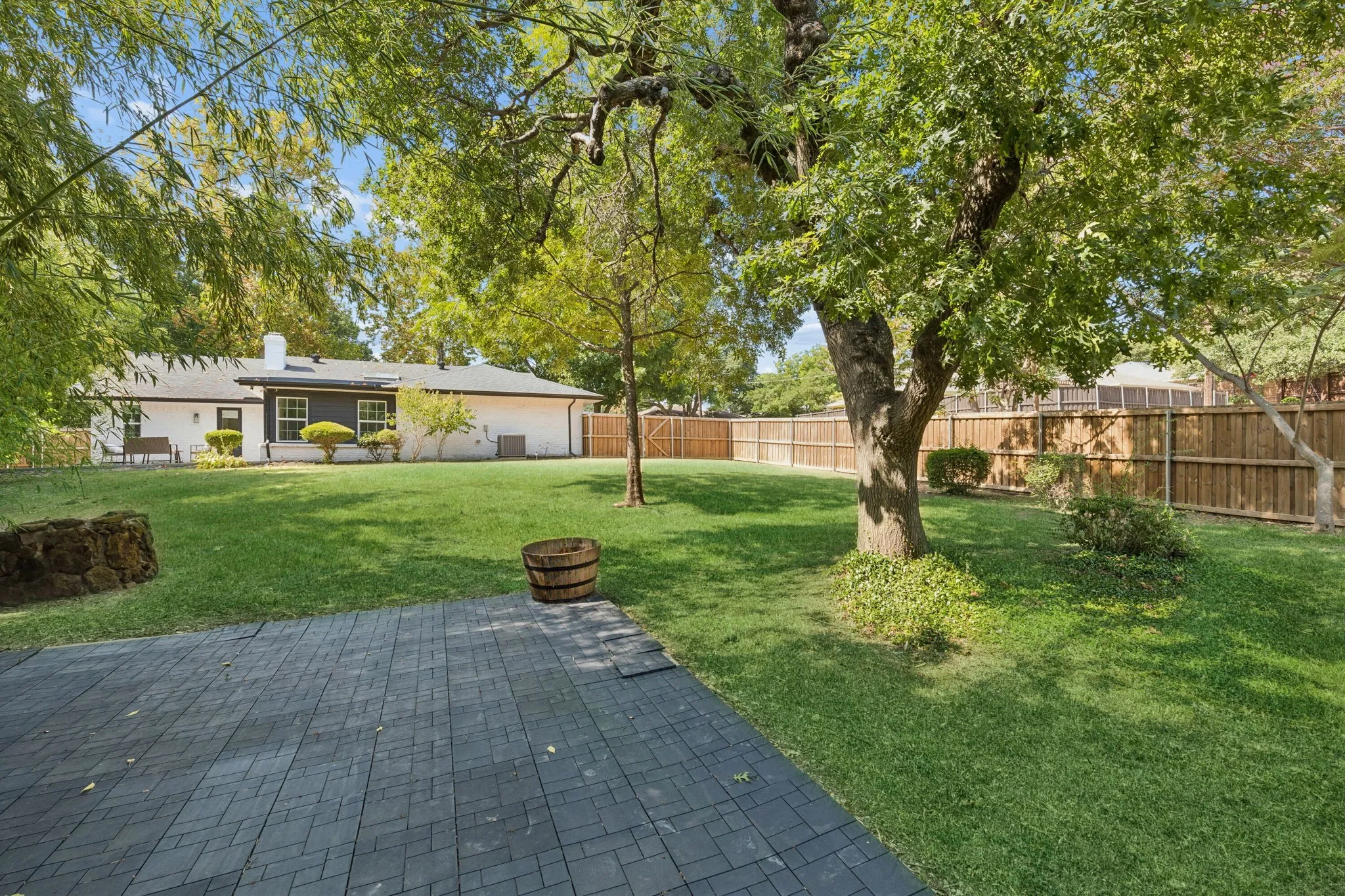 Expansive backyard with a patterned paver patio, established trees, and a wooden privacy fence