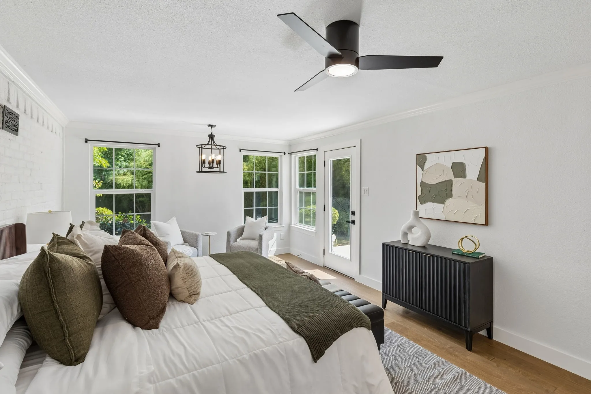 Wood-finish flooring, white painted brick wall, modern ceiling fan, multiple windows, and a glass-paned door