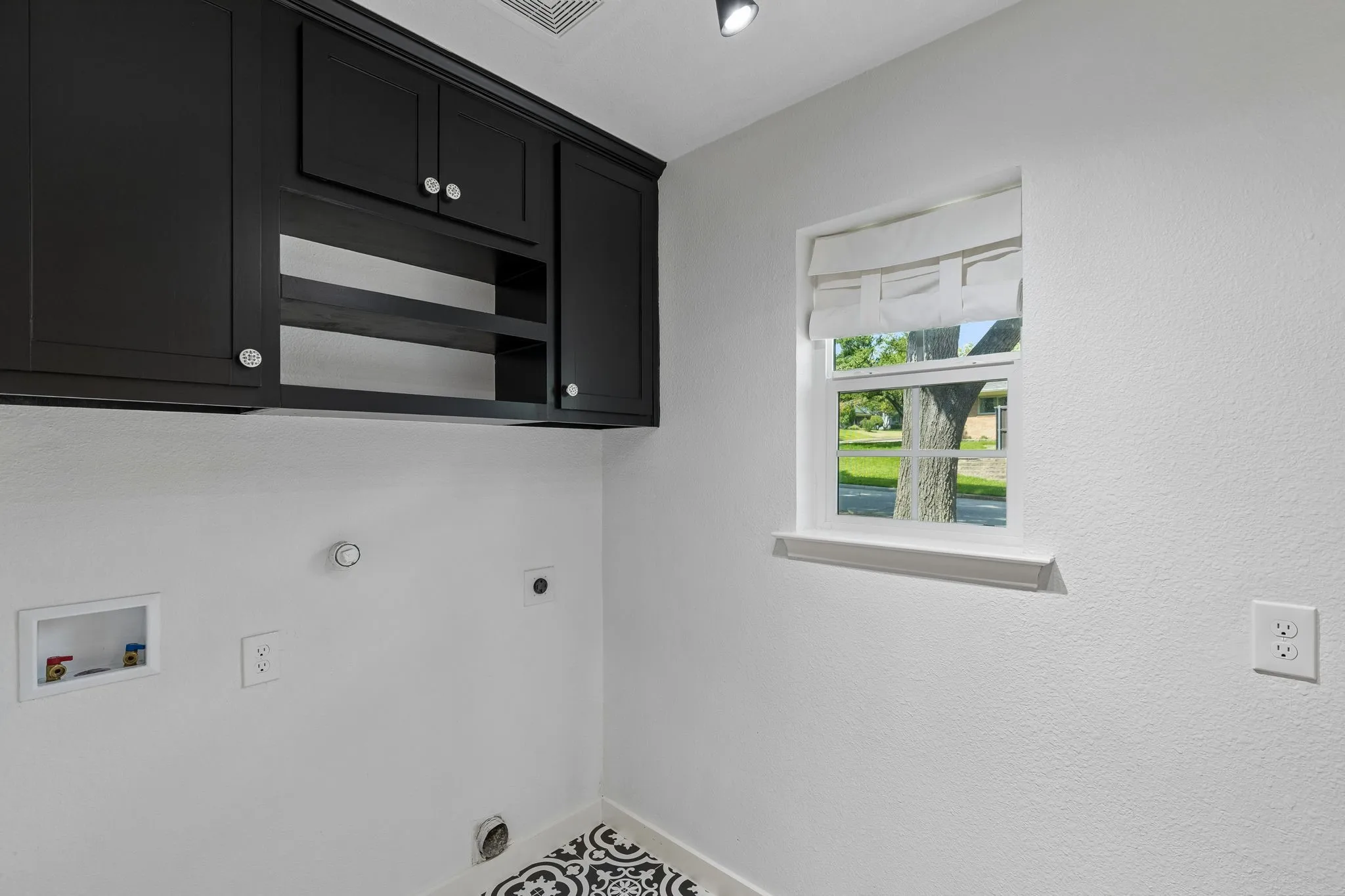 Black shaker-style cabinetry with built-in shelving, white walls, and a window with a fabric shade