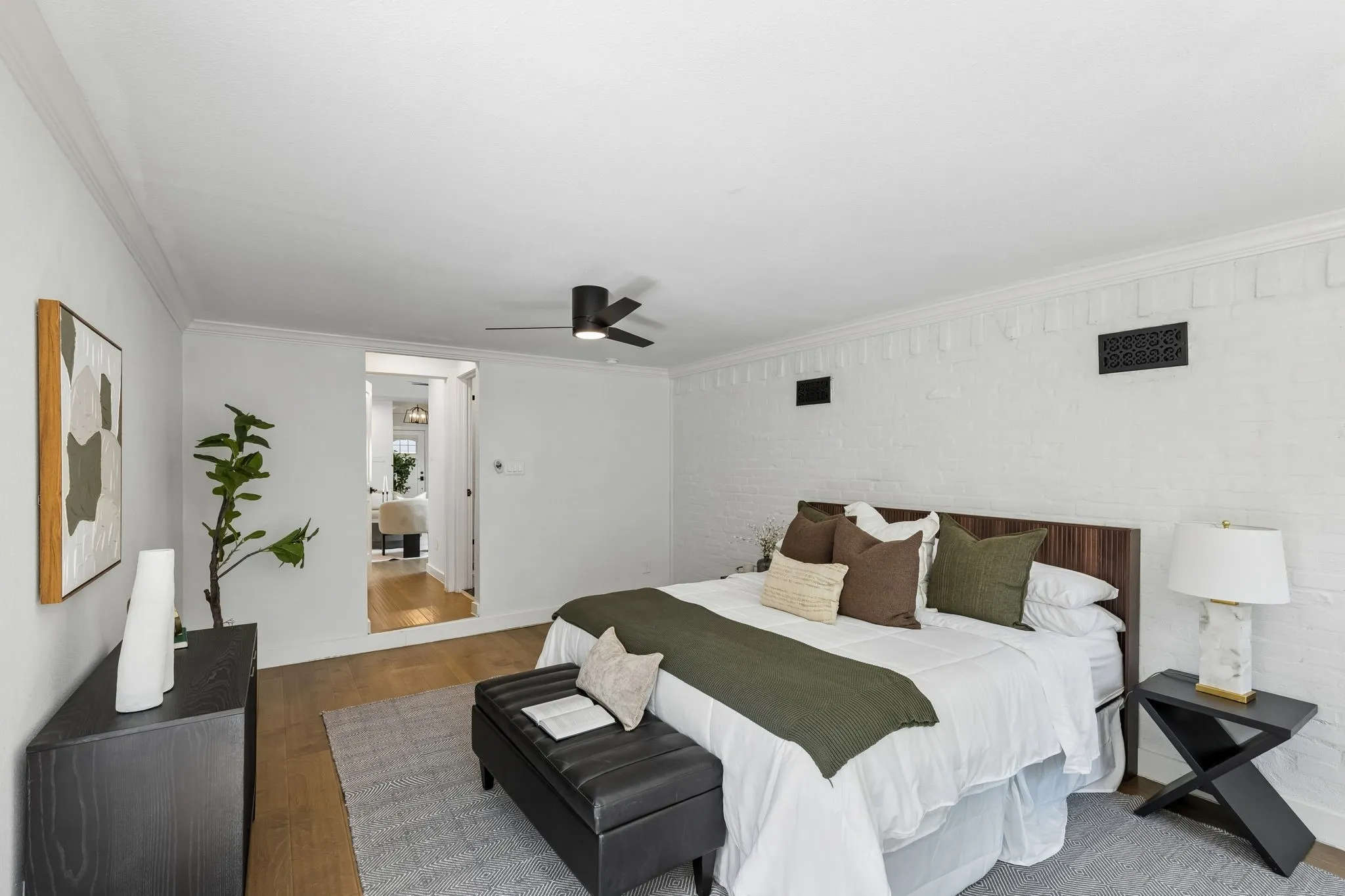 White painted brick wall, wood-finish flooring, ceiling fan, crown molding, and recessed doorway