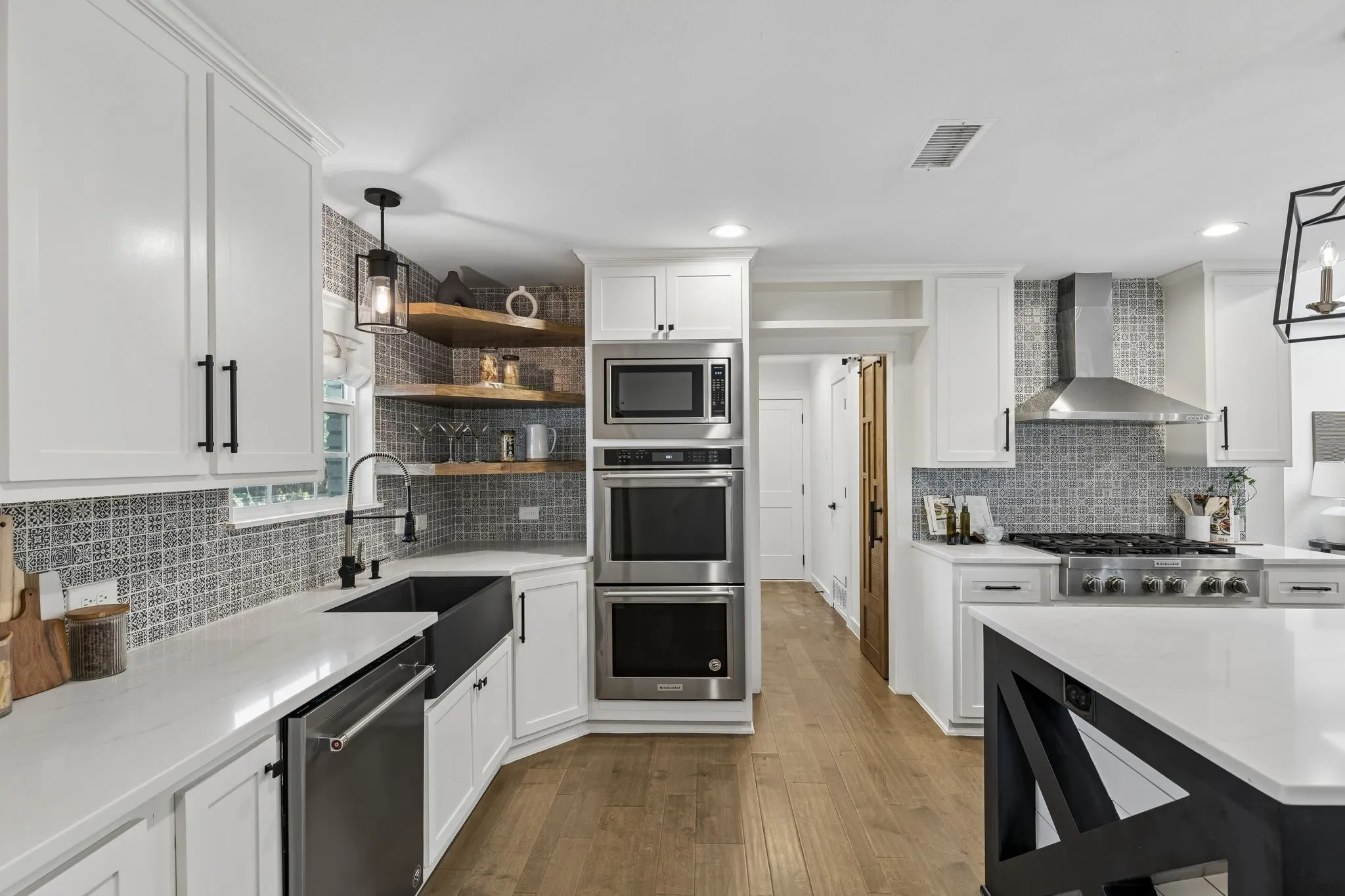 White cabinetry with black hardware, stainless steel appliances, patterned tile backsplash, wood-finish flooring, and white countertops