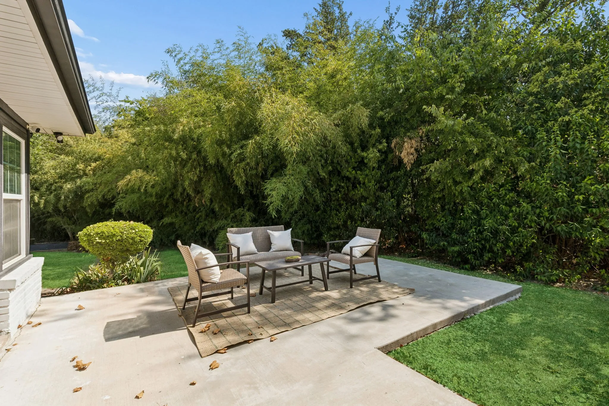 Expansive concrete patio with surrounding mature greenery and manicured lawn