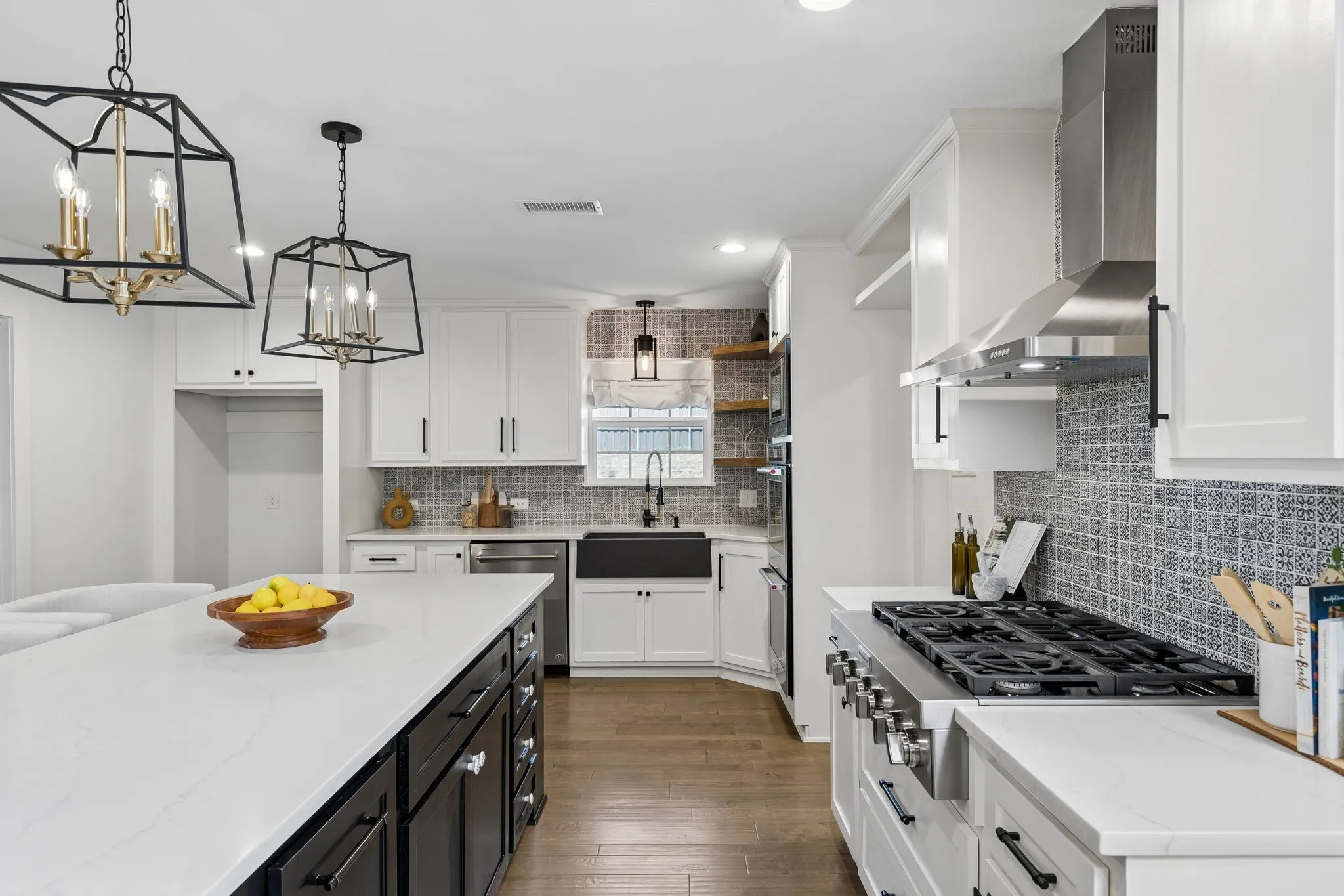 Kitchen featuring a large central island with a light-toned countertop, contrasting dark cabinetry, wood-finish flooring, white upper cabinetry, and a patterned tile backsplash
