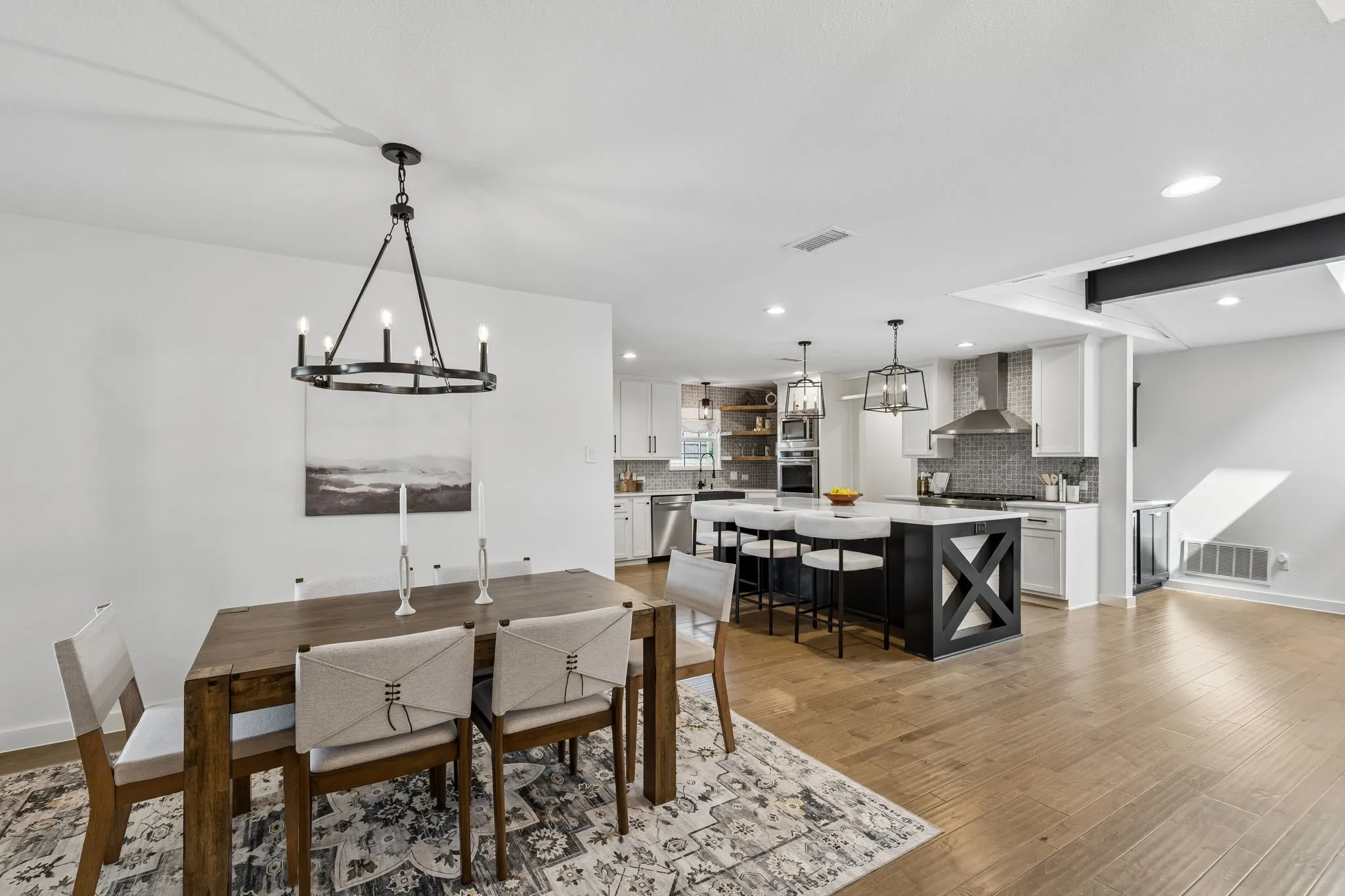 Hardwood-style flooring throughout, kitchen island with seating, stainless steel appliances, white cabinetry, and recessed lighting