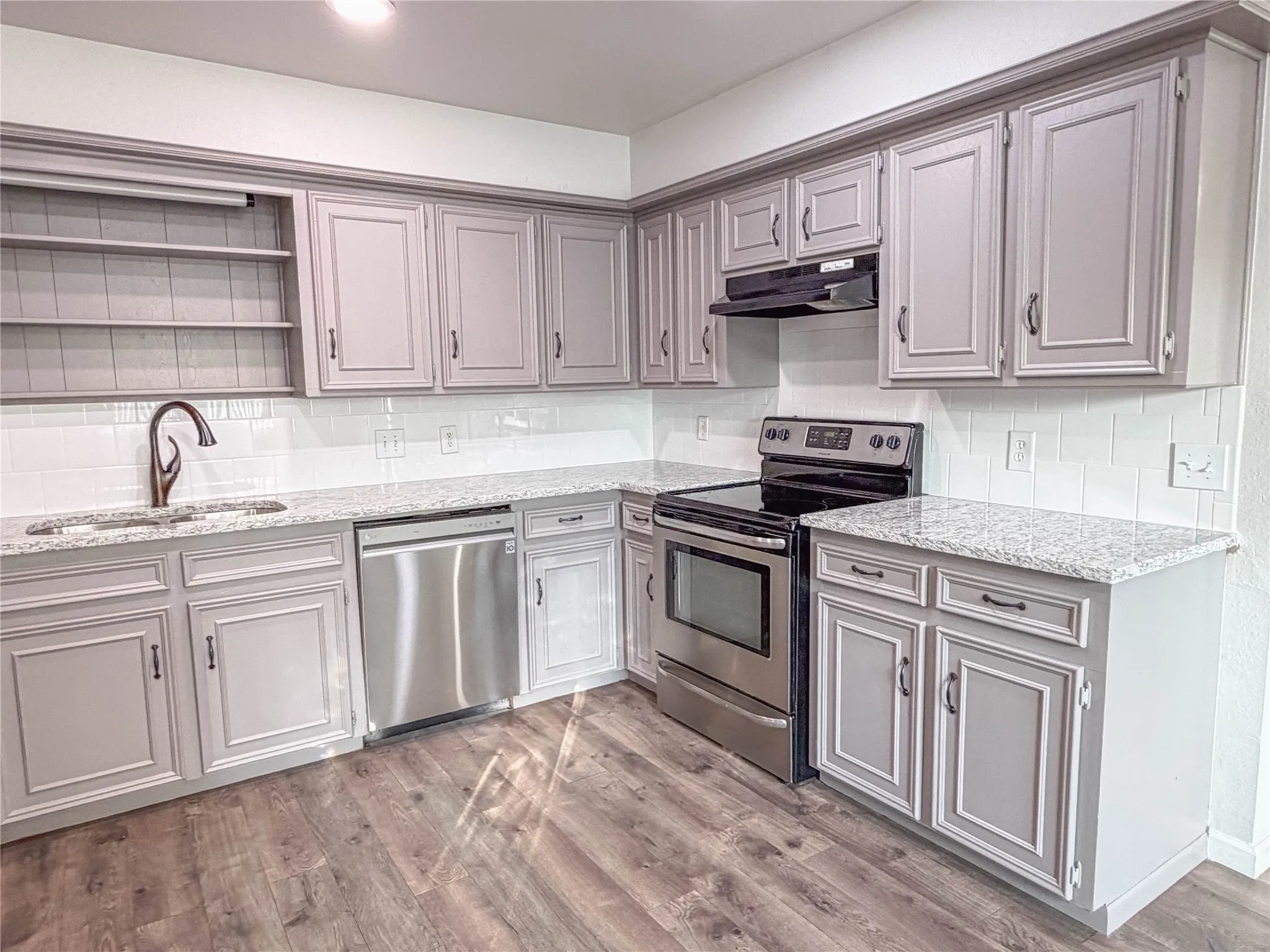 Kitchen featuring updated cabinetry, a tiled backsplash, granite countertops, stainless steel appliances, and wood-finish flooring