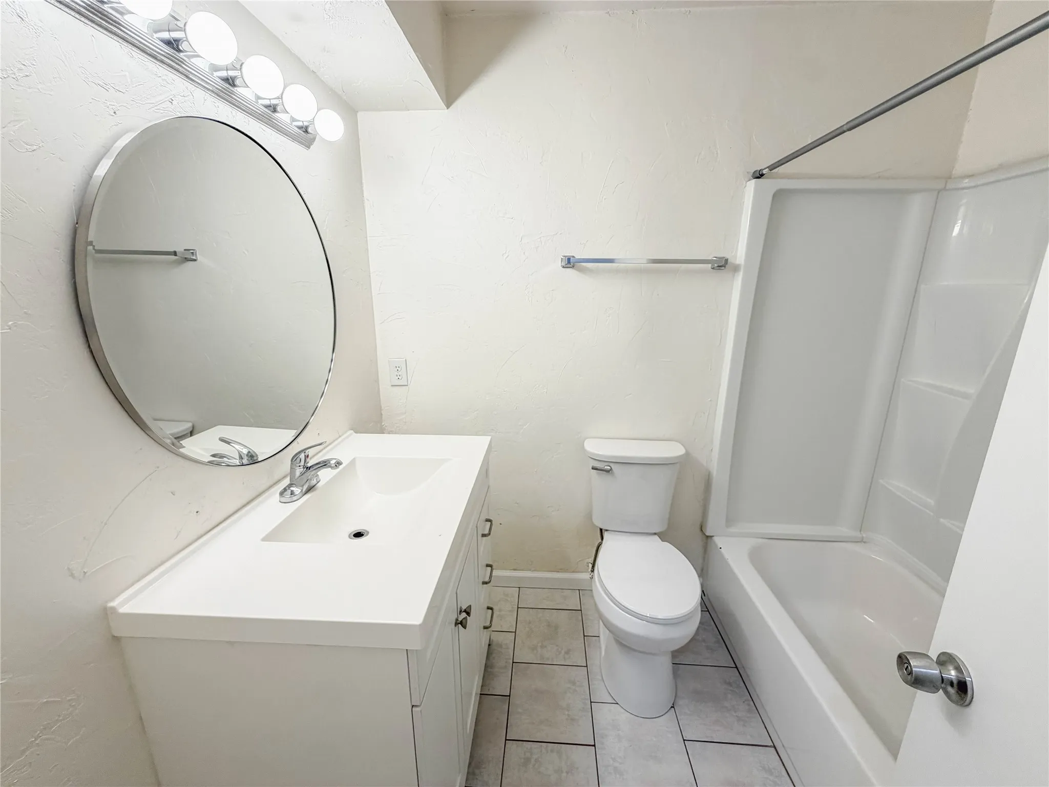Bathroom featuring a white vanity with integrated sink, chrome faucet, and round mirror