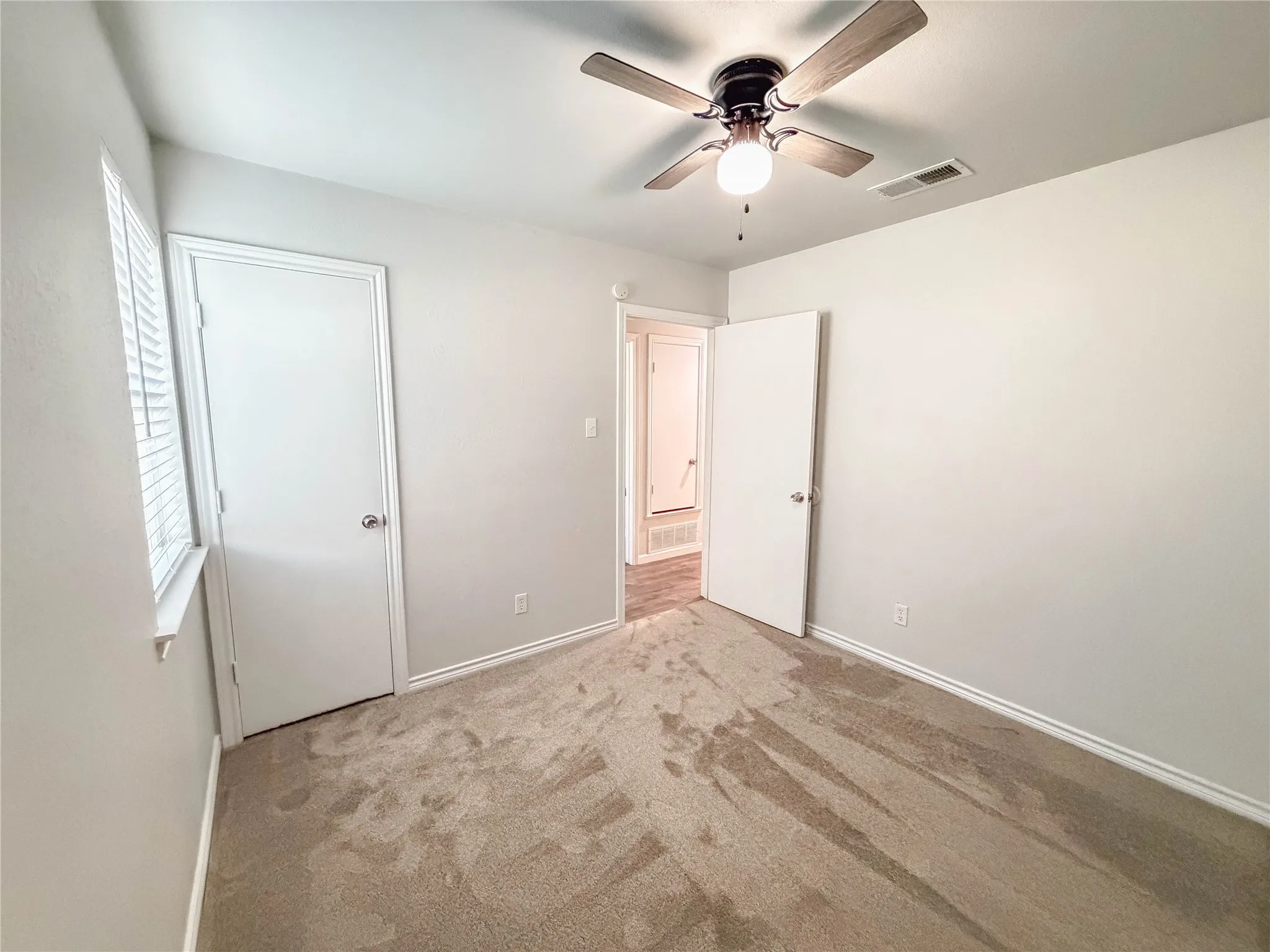 Recessed window with blinds, ceiling fan with integrated lighting, neutral wall paint, and two panel doors
