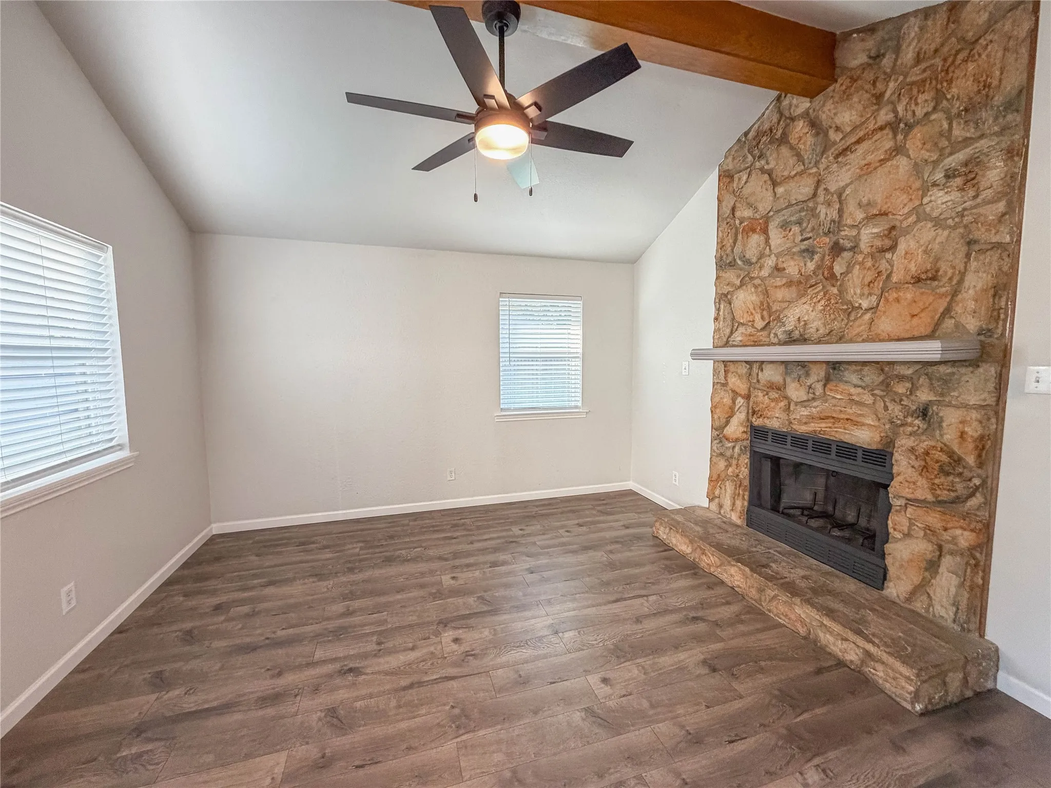 Stone-faced fireplace with hearth, wood-finish flooring, vaulted ceiling, and ceiling fan