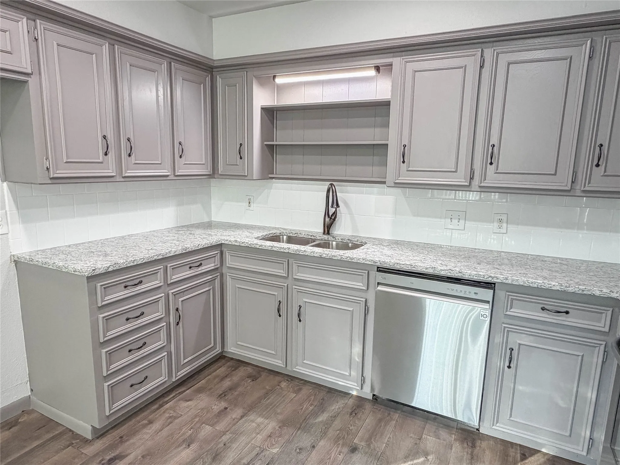 Kitchen featuring light gray cabinetry, light-toned countertops, white subway tile backsplash, stainless steel appliances, and wood-finish flooring