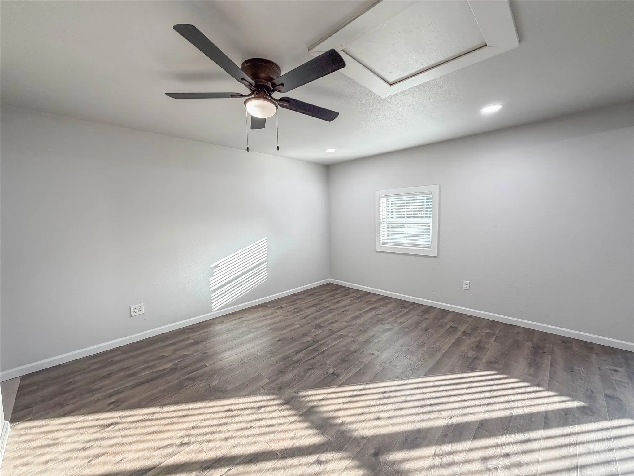 Wood-finish flooring, ceiling fan with integrated lighting, recessed ceiling lights, and a window with blinds