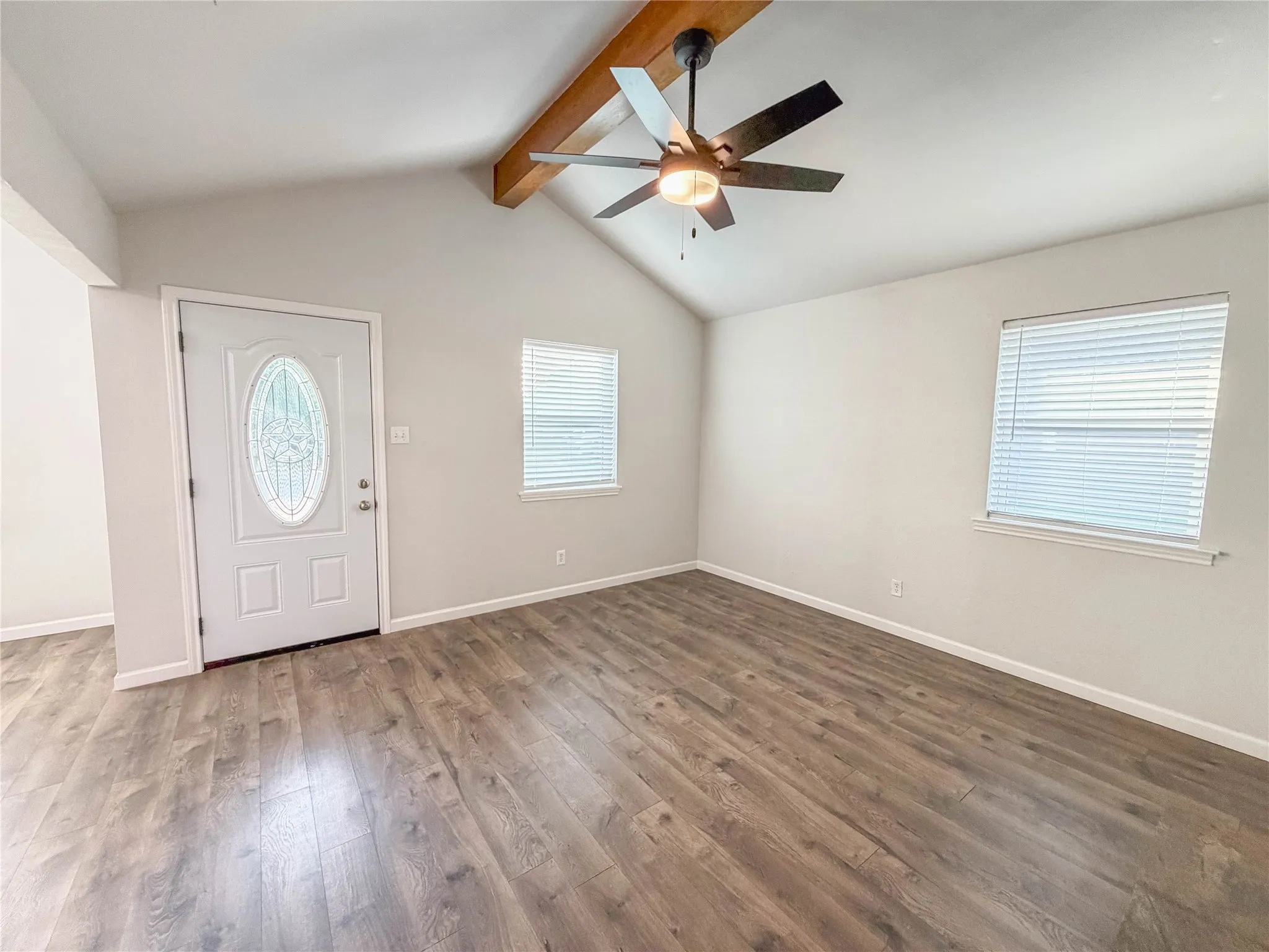 Vaulted ceiling with exposed wood-finish beam, wood-finish flooring, white paneled door with decorative glass insert, and window with blinds