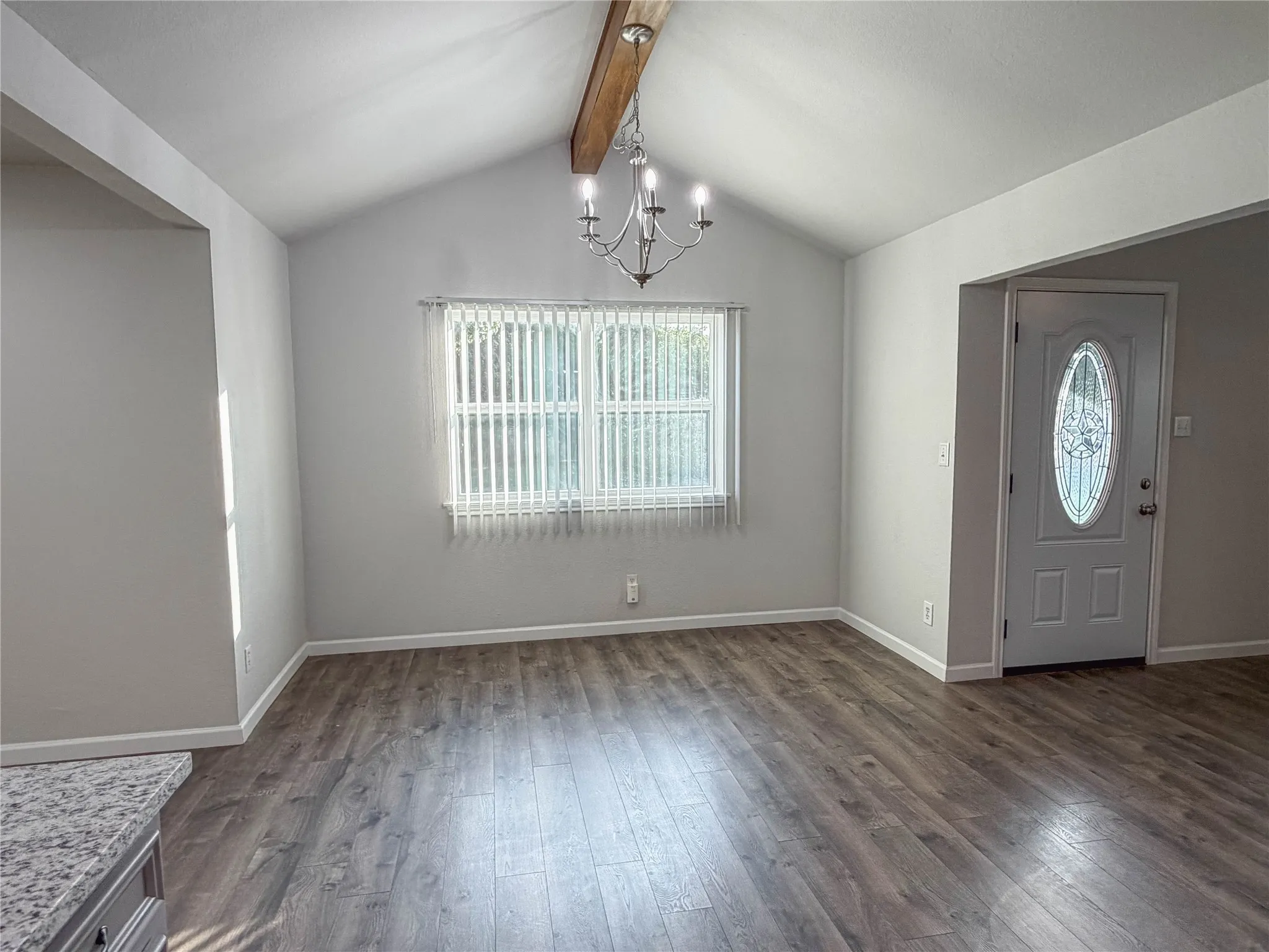 Vaulted ceiling with an exposed wood beam, wood-finish flooring, and a decorative front door with an oval glass insert
